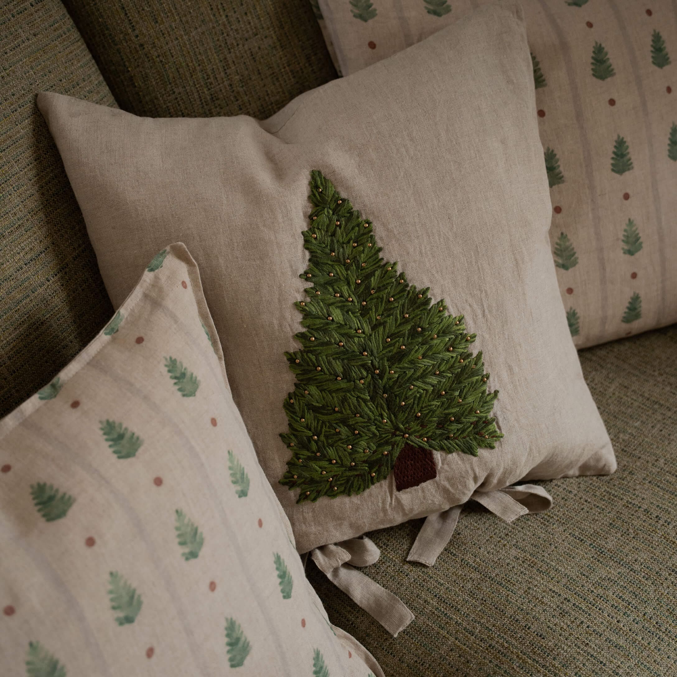 Beiges Leinenkissen mit grün besticktem Baum und dekorativen Perlen auf Sofa