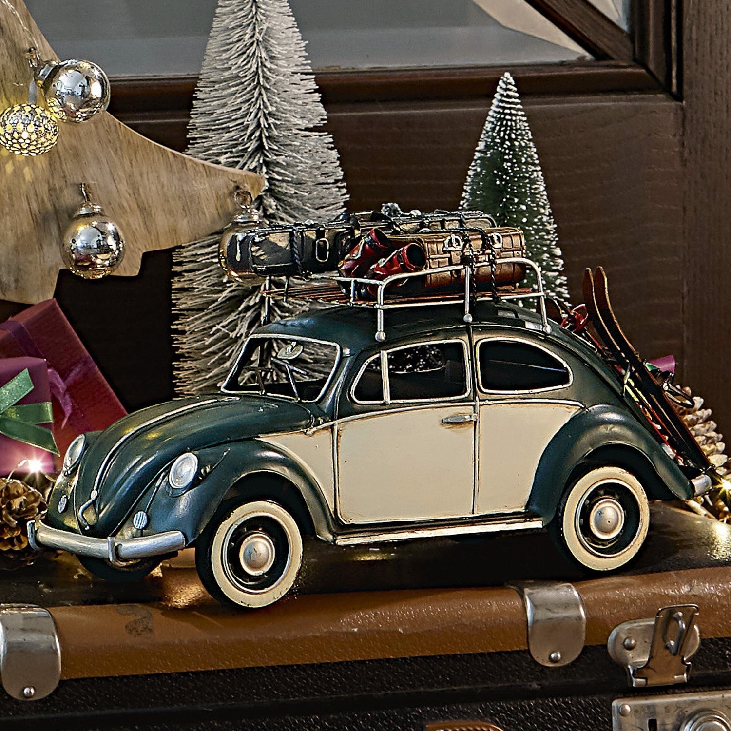 Deko-Auto Dawlish Modell eines grün-cremefarbenen Autos mit Metallgepäckträger und Skiern vor Weihnachtsdekoration