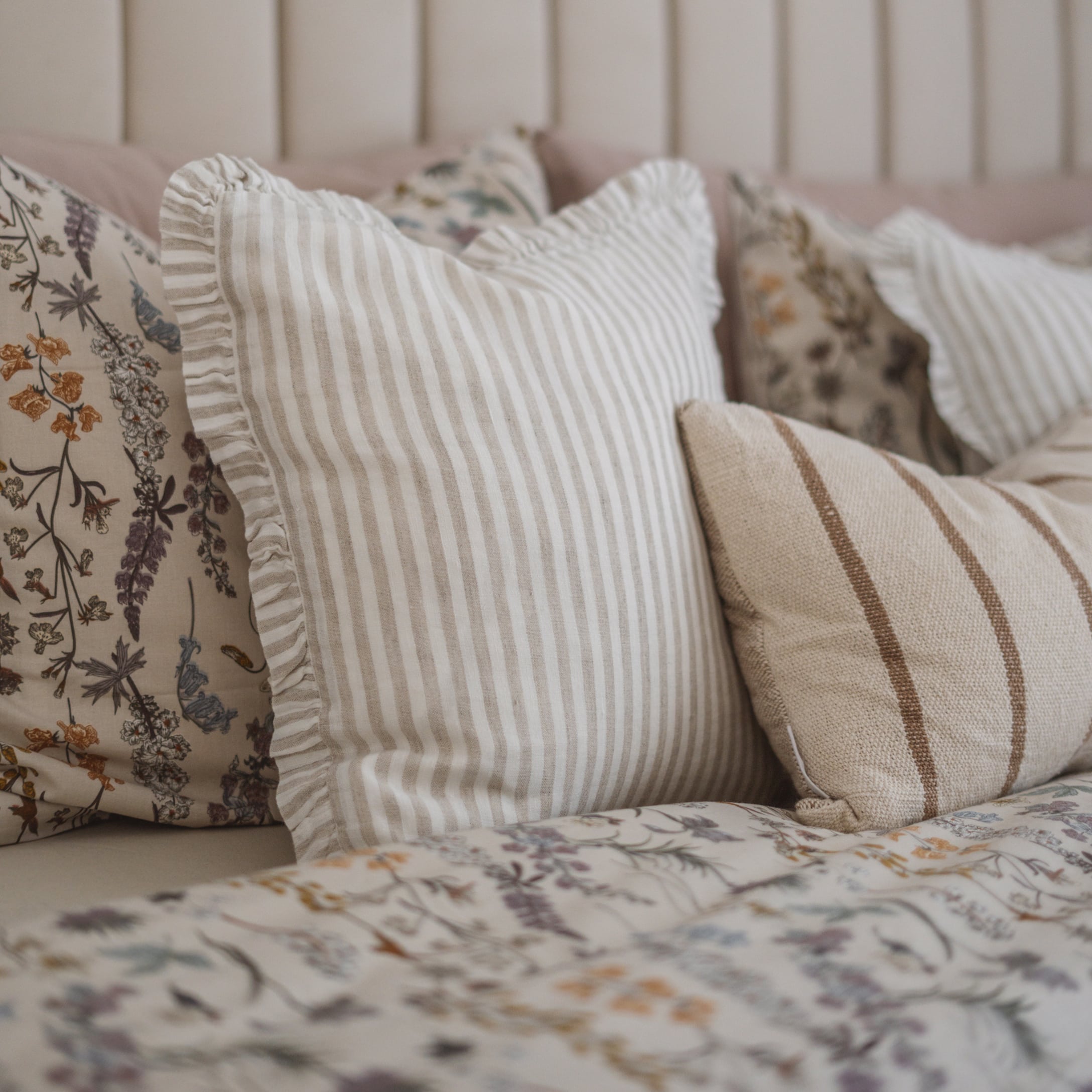 Dekorative Kissen mit beigen Streifen und floralem Muster auf dem Bett im Schlafzimmer