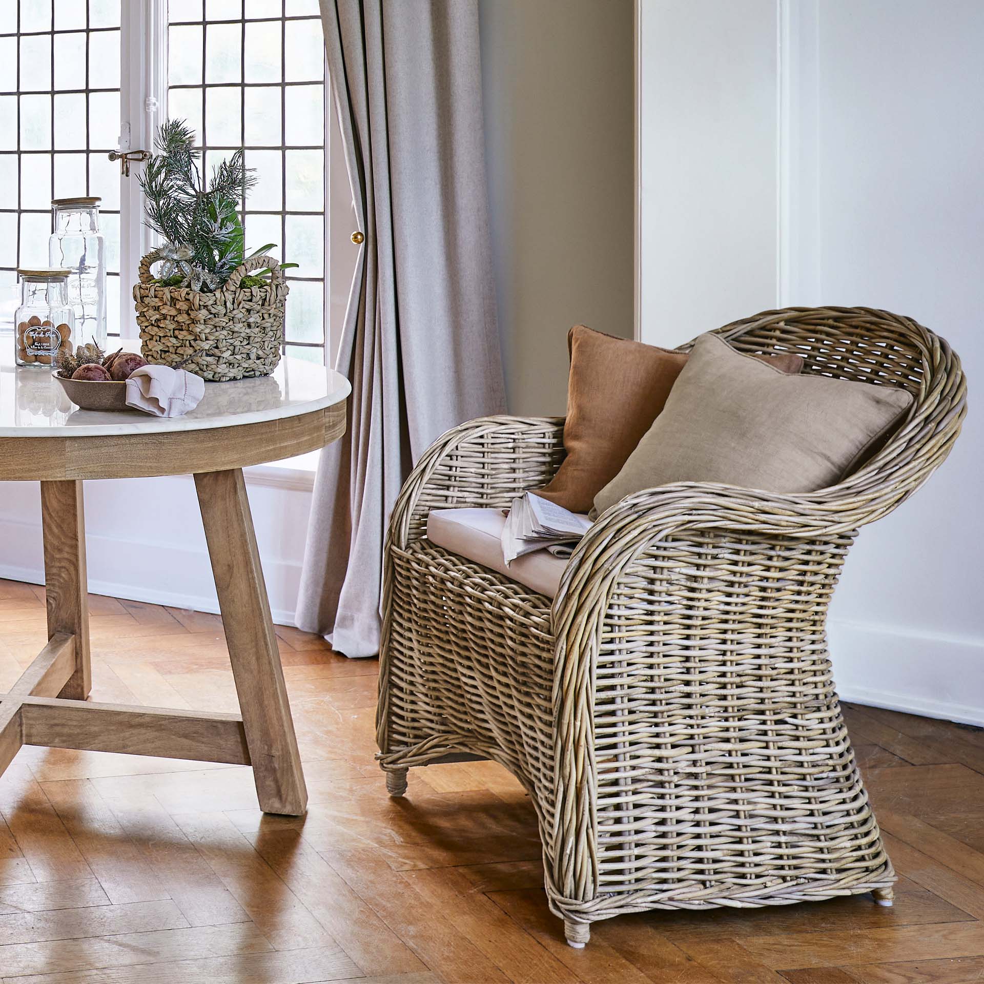 Natürlicher Rattansessel mit beigen Kissen in hellem Wohnzimmer mit Holzboden
