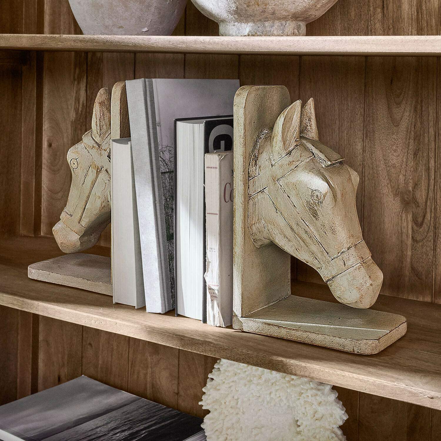 Buchstütze 2er Set Caravena Paar beige Holz-Buchstützen in Pferdekopf-Form auf einem Regal mit Büchern