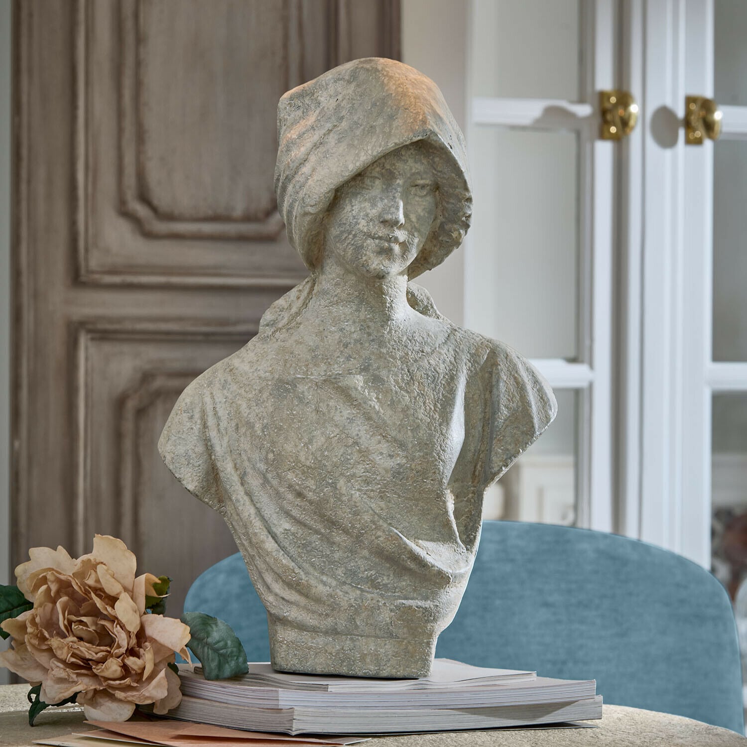 Büste Mireline Graue Steinstatue einer Frau als Büste auf einem Bücherstapel mit dekorativer Blume daneben