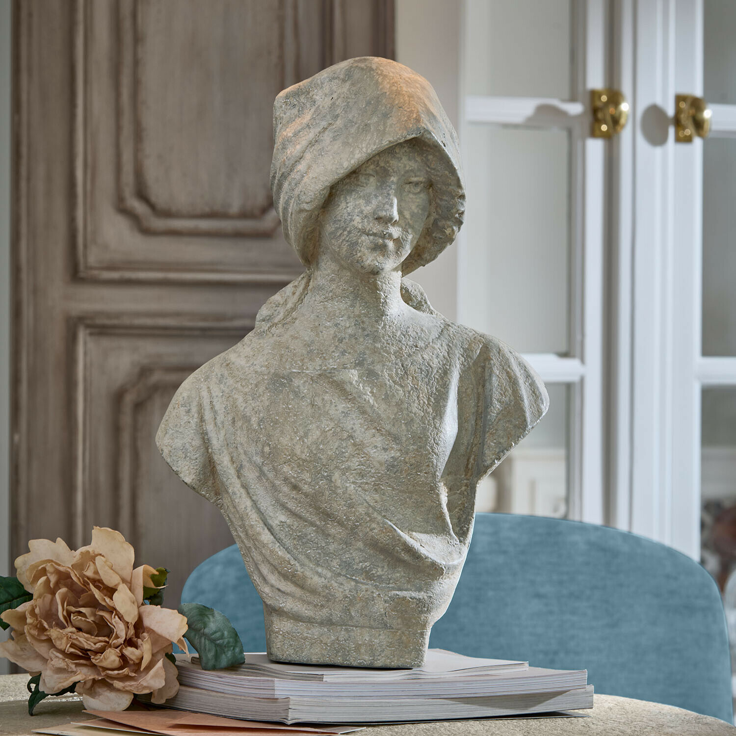Büste Mireline Graue Steinstatue einer Frau als Büste auf einem Bücherstapel mit dekorativer Blume daneben