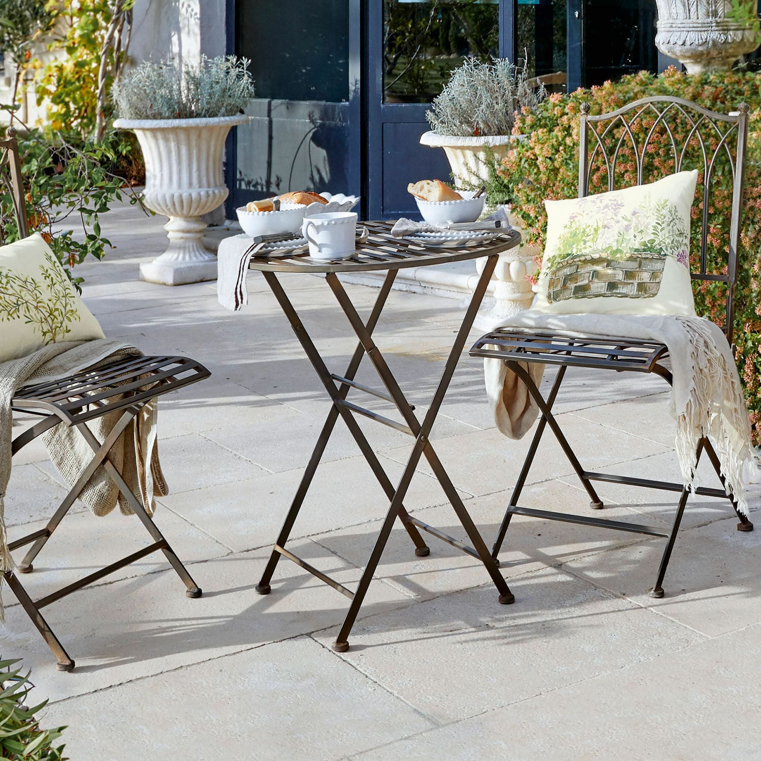 Tisch Brignoles Brauner Metall-Klapptisch und Stühle auf der Terrasse mit dekorativen Kissen und weissem Geschirr