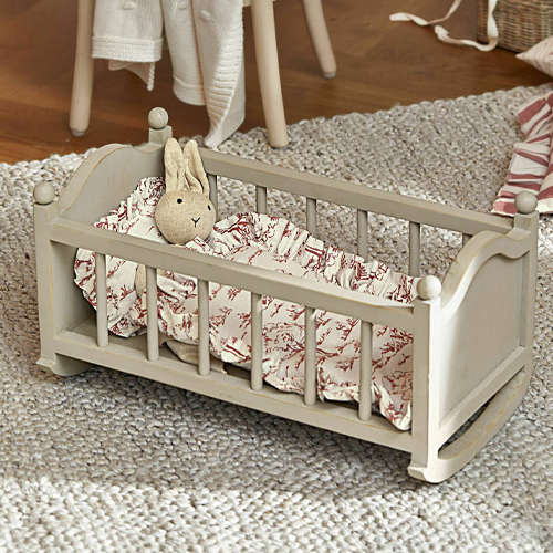 Graues Holzpuppenbett mit Plüschhase und gemusterter Bettwäsche auf Teppichboden