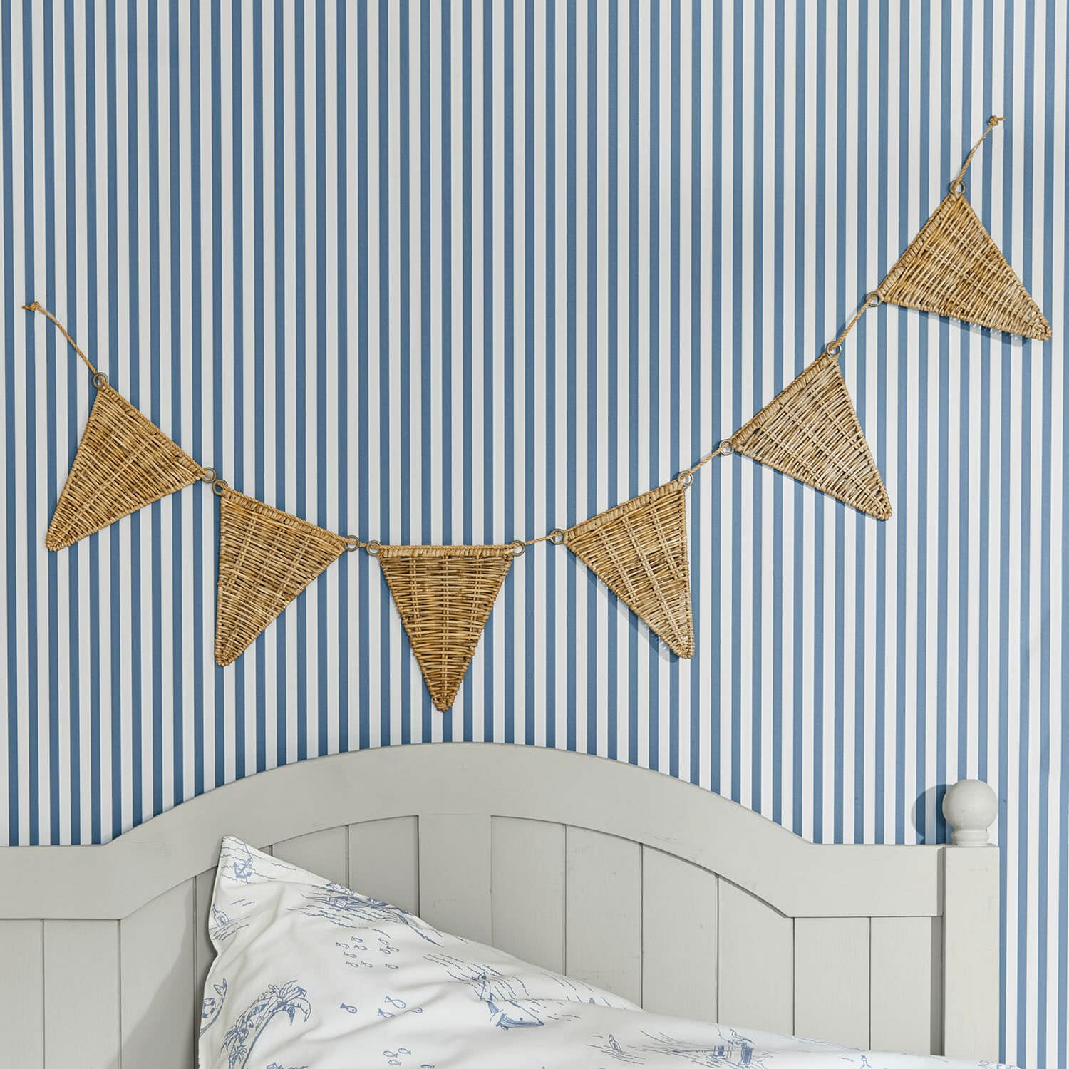 Wimpelgirlande Anglemont Dekorative Wimpelkette aus geflochtenem Rattan an blau-weiss gestreifter Wand im Schlafzimmer