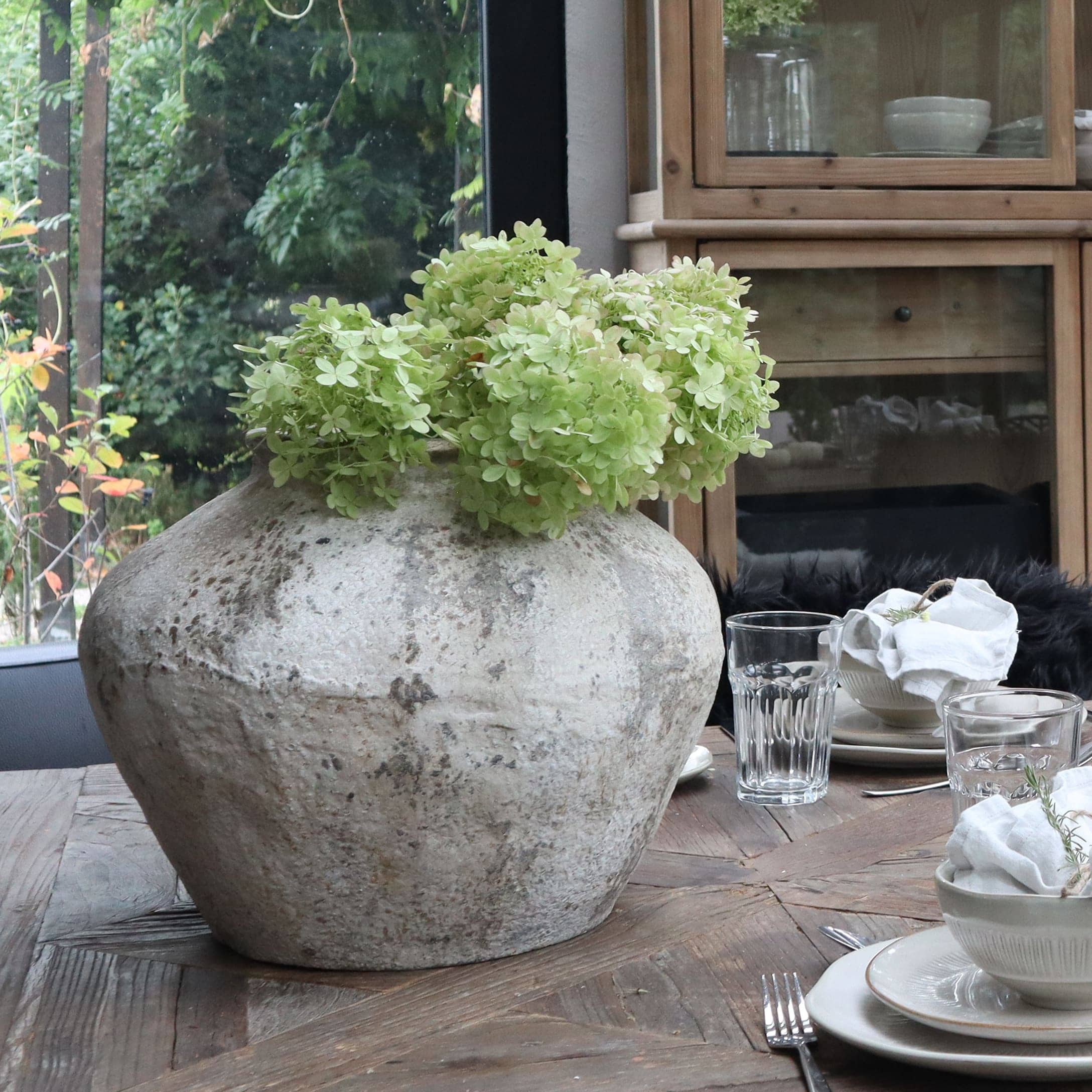 Grosse graue Keramikvase mit grünen Blumen auf Holztisch im Esszimmer