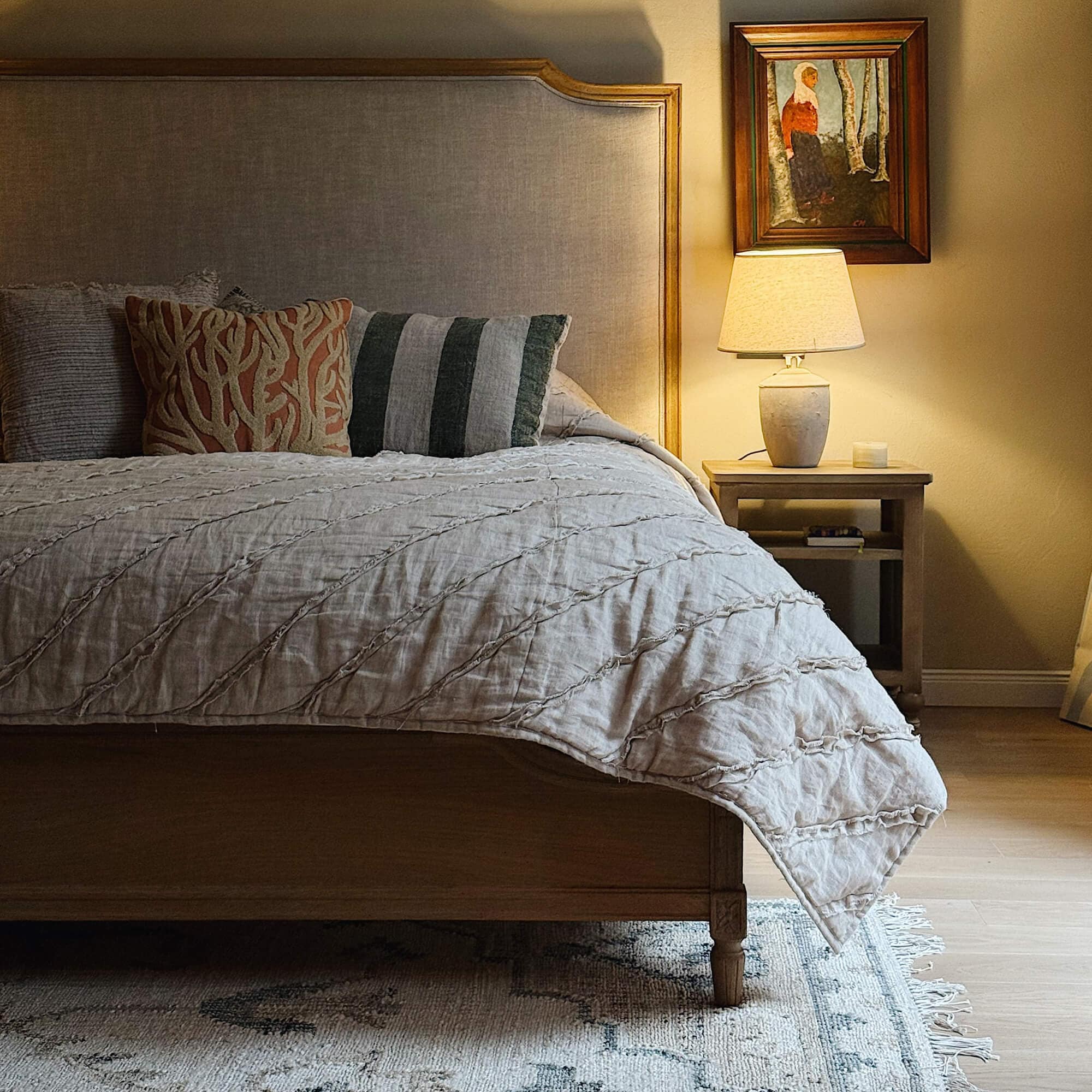 Gemütliches Schlafzimmer mit Holzbett, beiger Tagesdecke und Lampe auf Holz-Nachttischchen