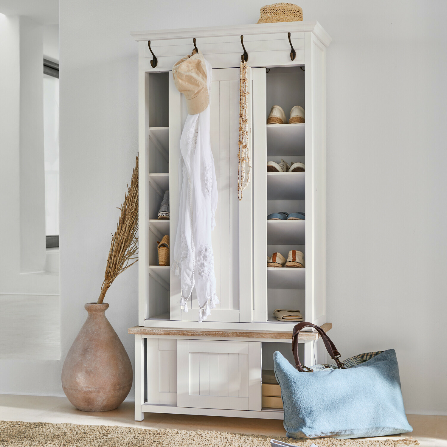 Weisse Holzschuhschrank mit Haken und Regalen, blaue Tasche und Strohhut als Dekoration