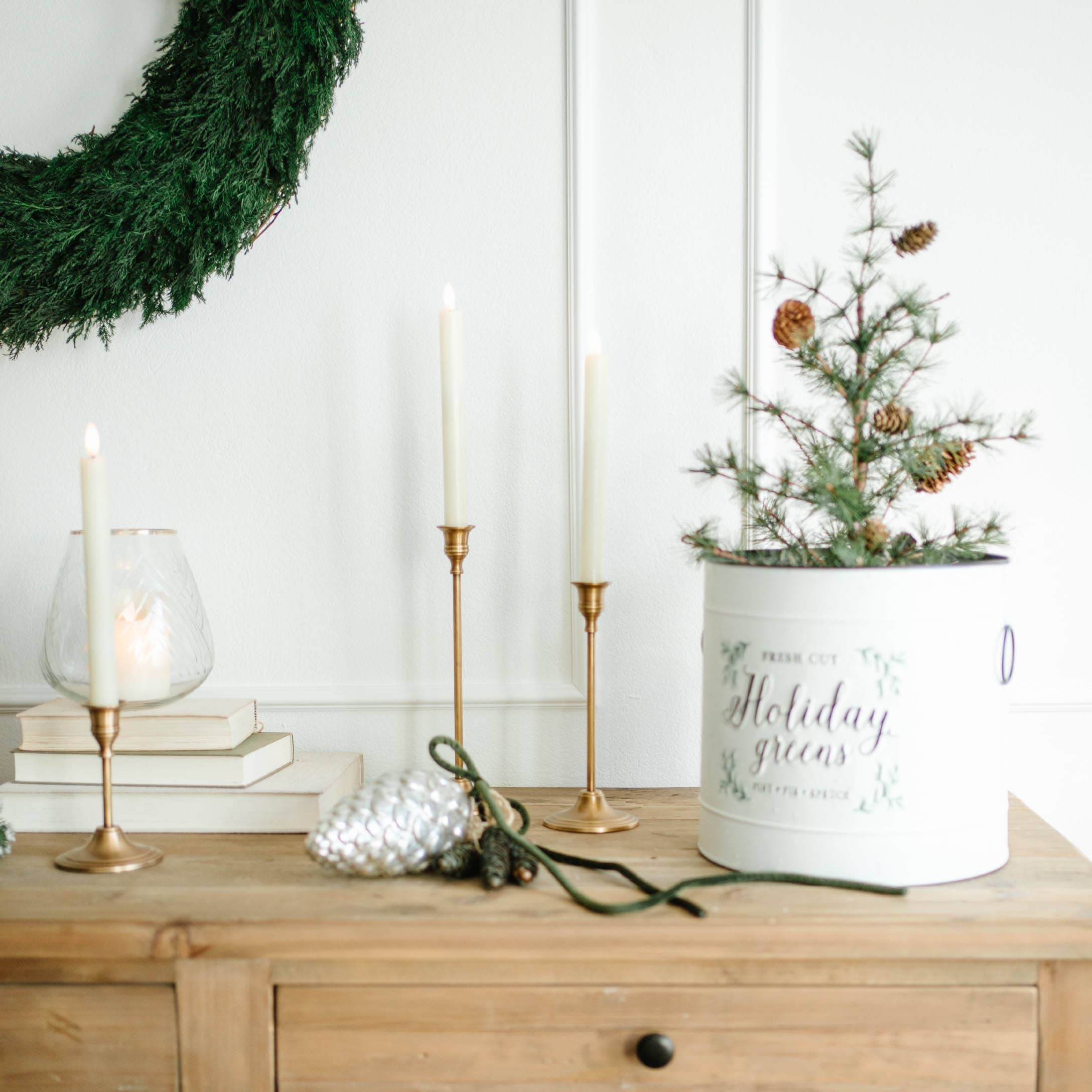 Weihnachtsdekoration mit grünem Kranz, goldenen Kerzenhaltern und weissem Behälter mit Zweigen und Zapfen