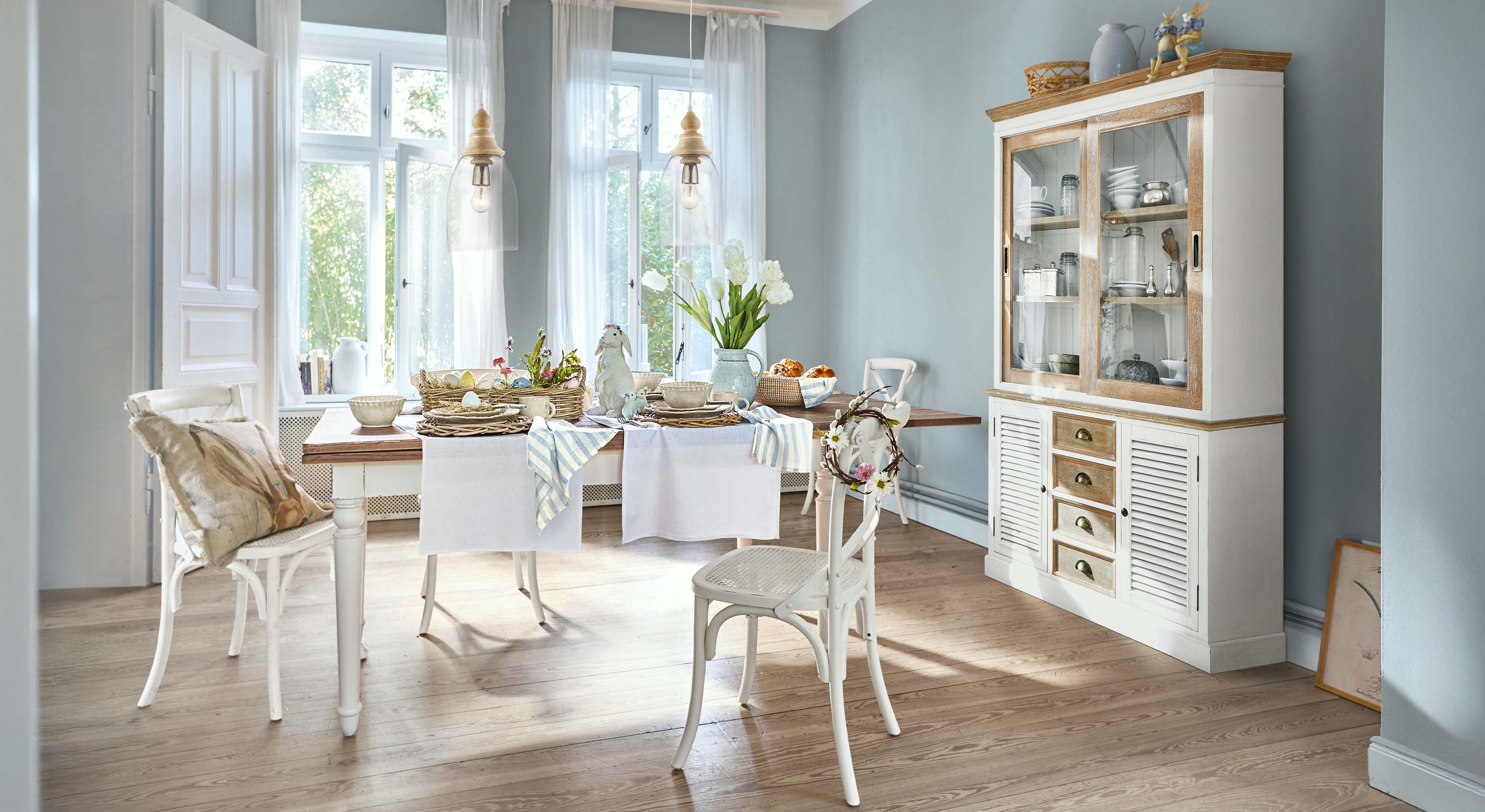 Esszimmer mit weissem Holztisch und Stühlen, Osterdekorationen und Vitrine mit Glastüren aus hellem Holz