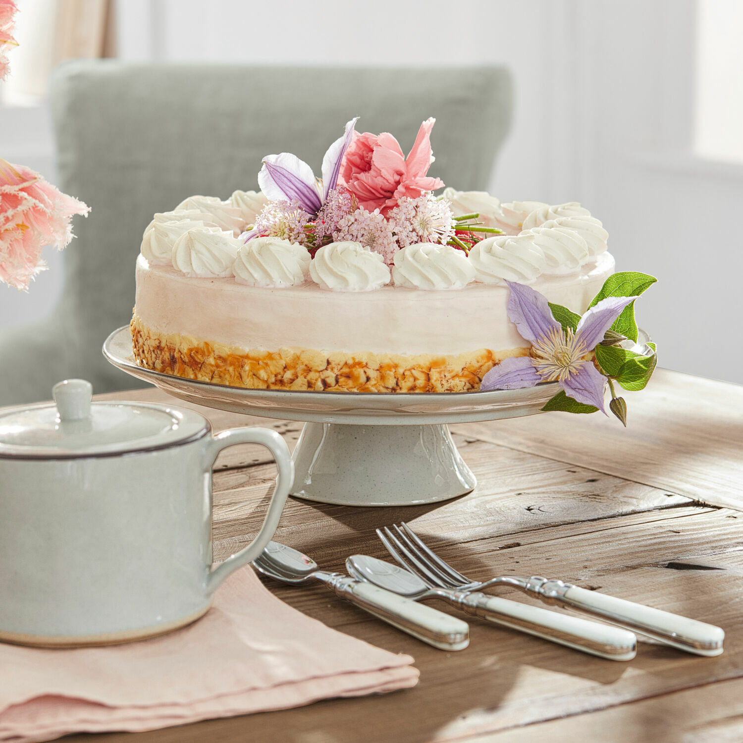 Platte Biarré Kuchen auf Keramik-Tortenplatte mit Creme und Blumen, weisse Besteckgriffe auf Holztisch