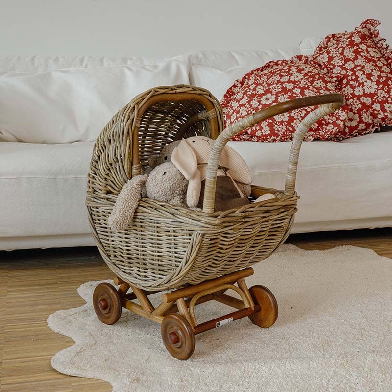Kinderwagen aus Weide mit Holzrädern und Plüschtieren vor weissem Sofa in hellem Raum