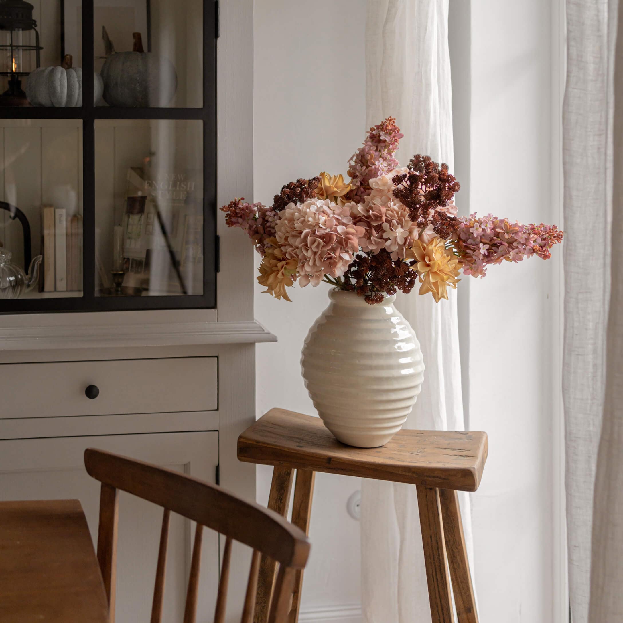Weisse Alabastervase mit gelb-rosa Blumen auf Holzschemel in hellem Raum