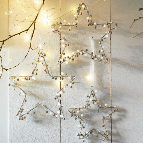 Dekorative Metallsterne mit weissen Glöckchen und LED-Lichtern als Weihnachtsdekoration an der Wand