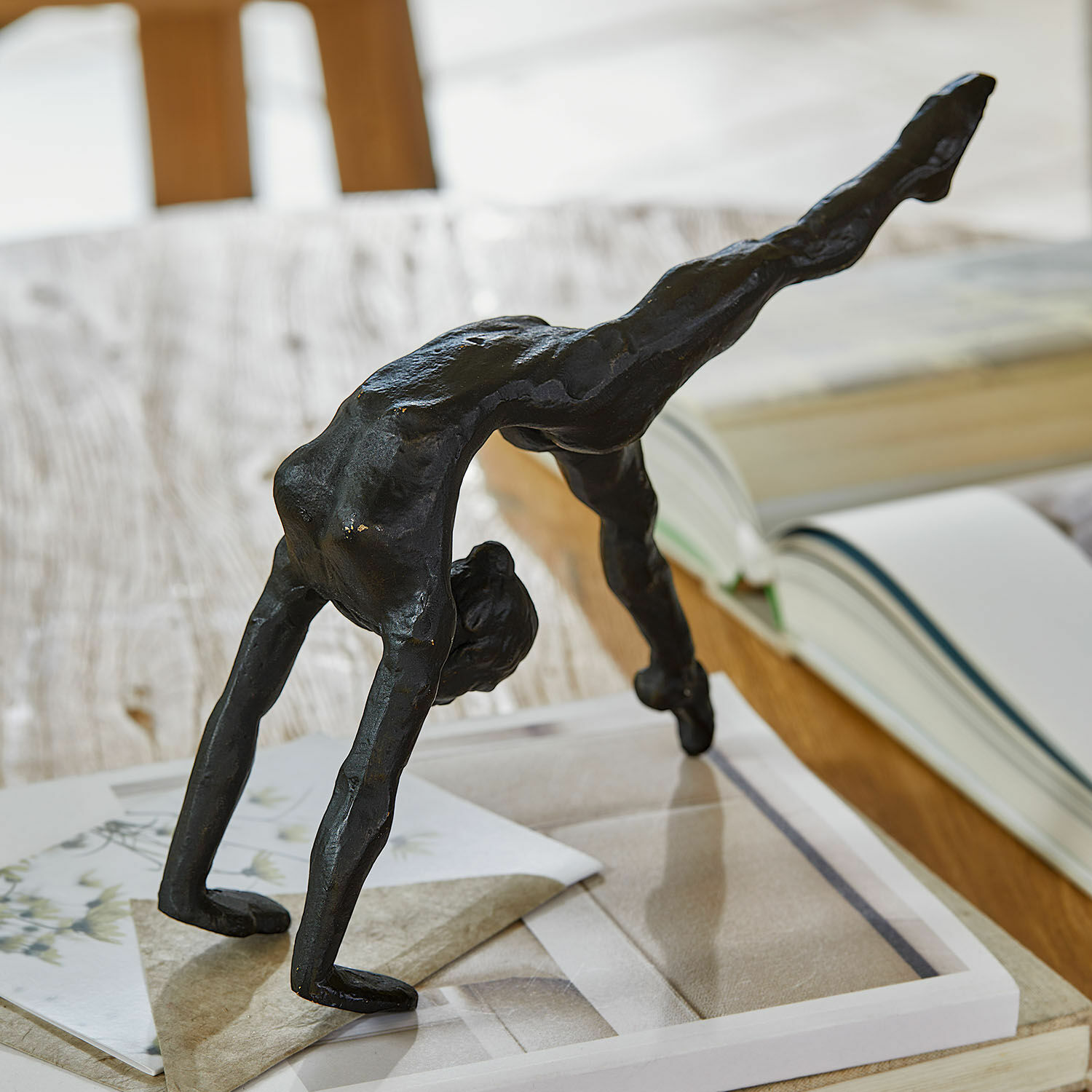 Figur Zayrah Schwarze Metallfigur eines Akrobaten in Brückenposition auf einem Tisch mit Büchern und Papieren