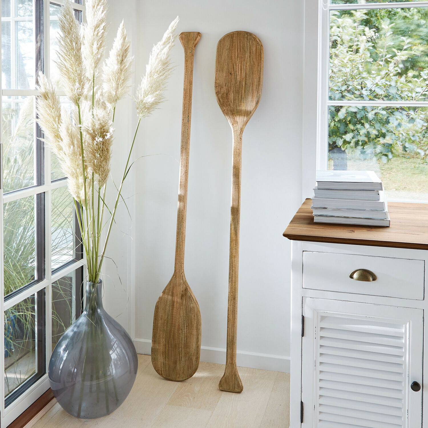 Zwei dekorative Holzpaddel in hellem Raum neben grauer Vase und weissem Schrank