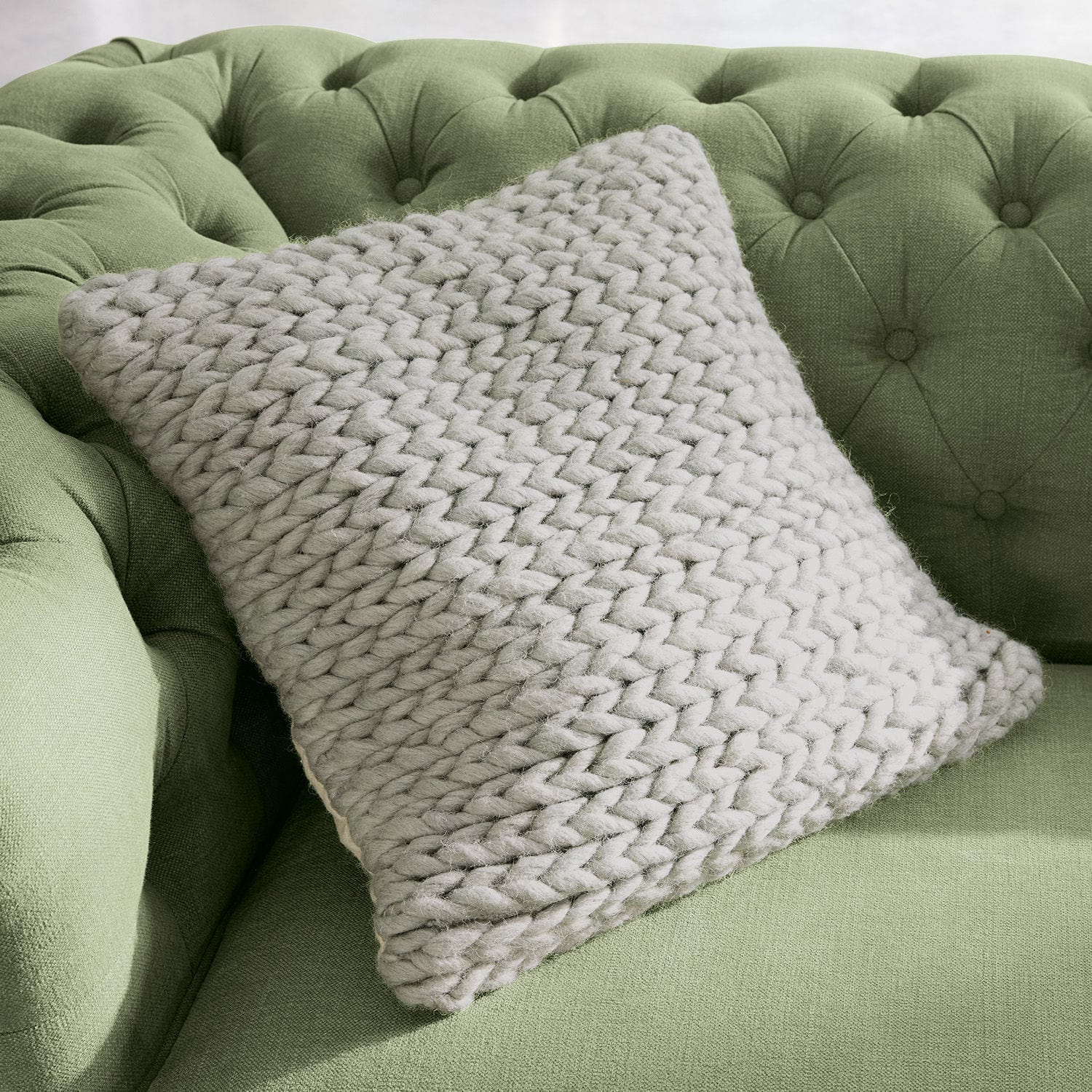 Kissenhülle Limnia Beiges Kissen mit grobem Strick aus weicher Wolle auf grünem, gepolstertem Sofa