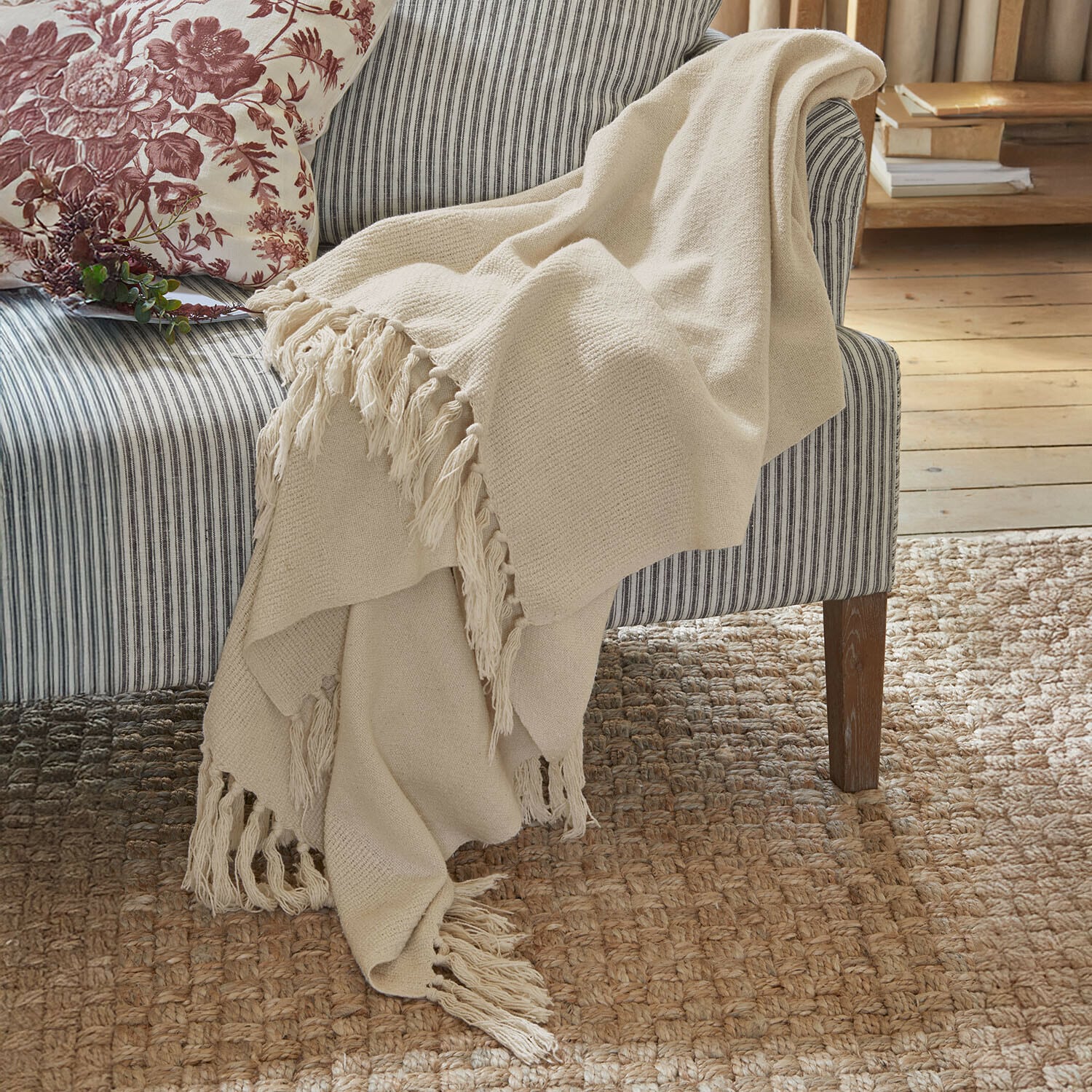 Plaid Skandira Beige Kuscheldecke mit Fransen aus weichem Stoff auf grauem, gestreiftem Sofa in gemütlichem Raum