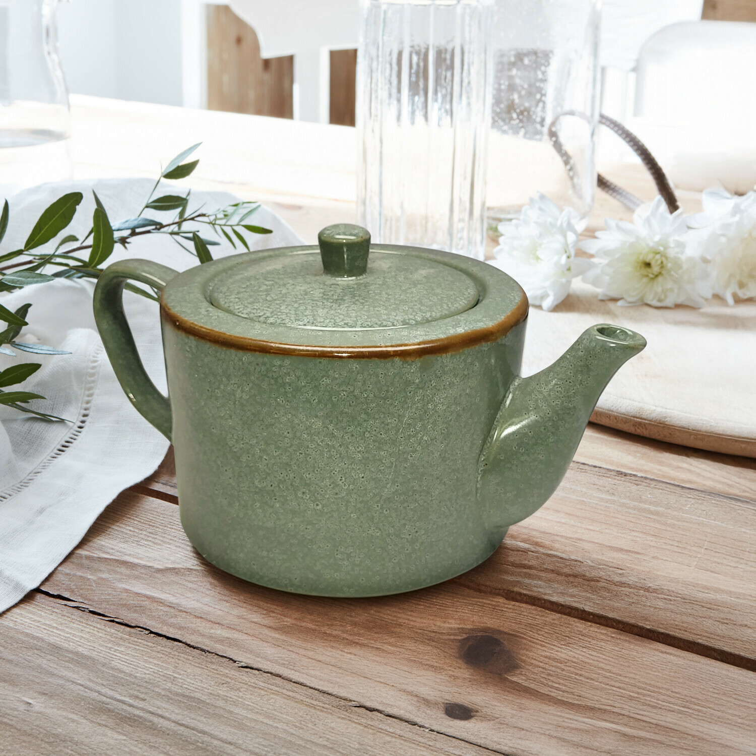 Teekanne Biarré Grüner Keramik-Teekessel mit Deckel und braunem Rand auf Holztisch mit Blumenarrangement