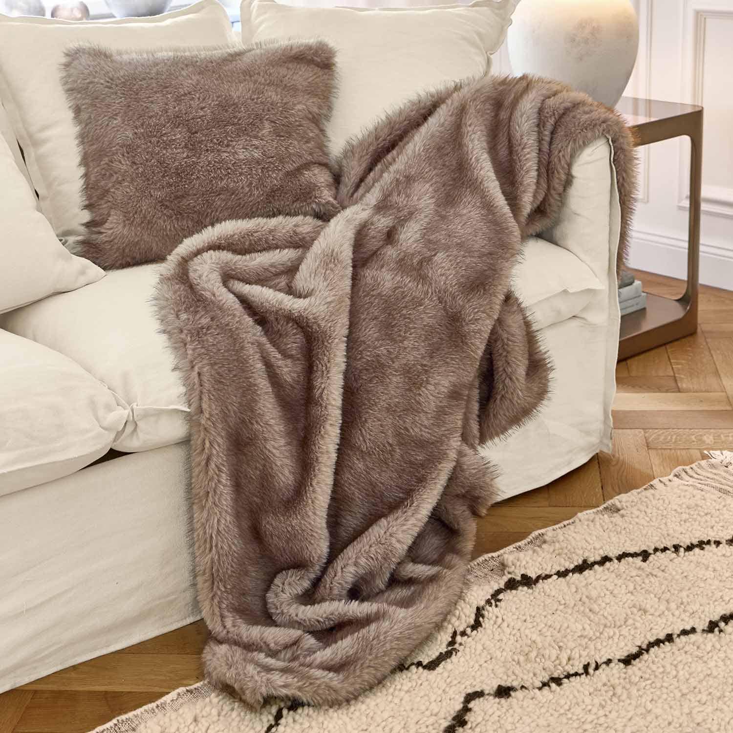 Weiche braune Kunstfell-Decke und Kissen auf weissem Sofa in gemütlichem Wohnzimmer