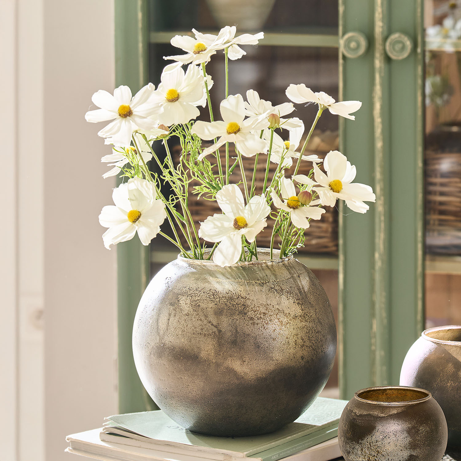 Runder silberner Metallvase mit weissen Blumen auf Büchern, elegante Wohnraumdekoration