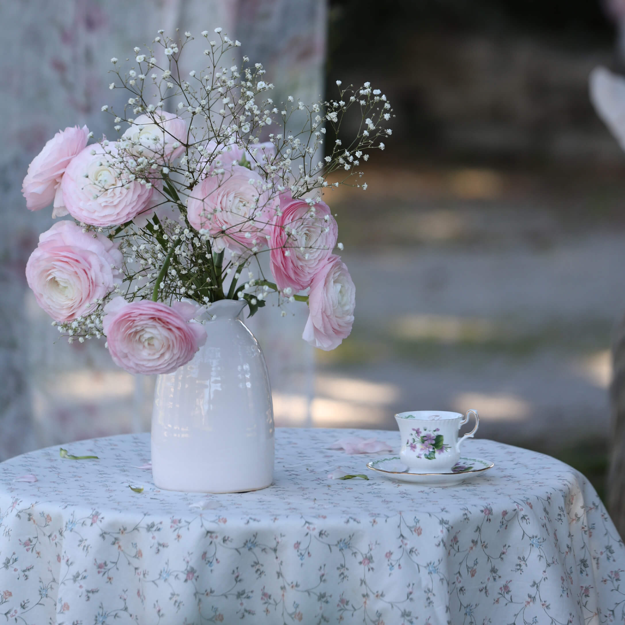 Strauß aus rosa und weißen Blumen in weissem Keramikvase auf Tisch mit floralem Tischtuch