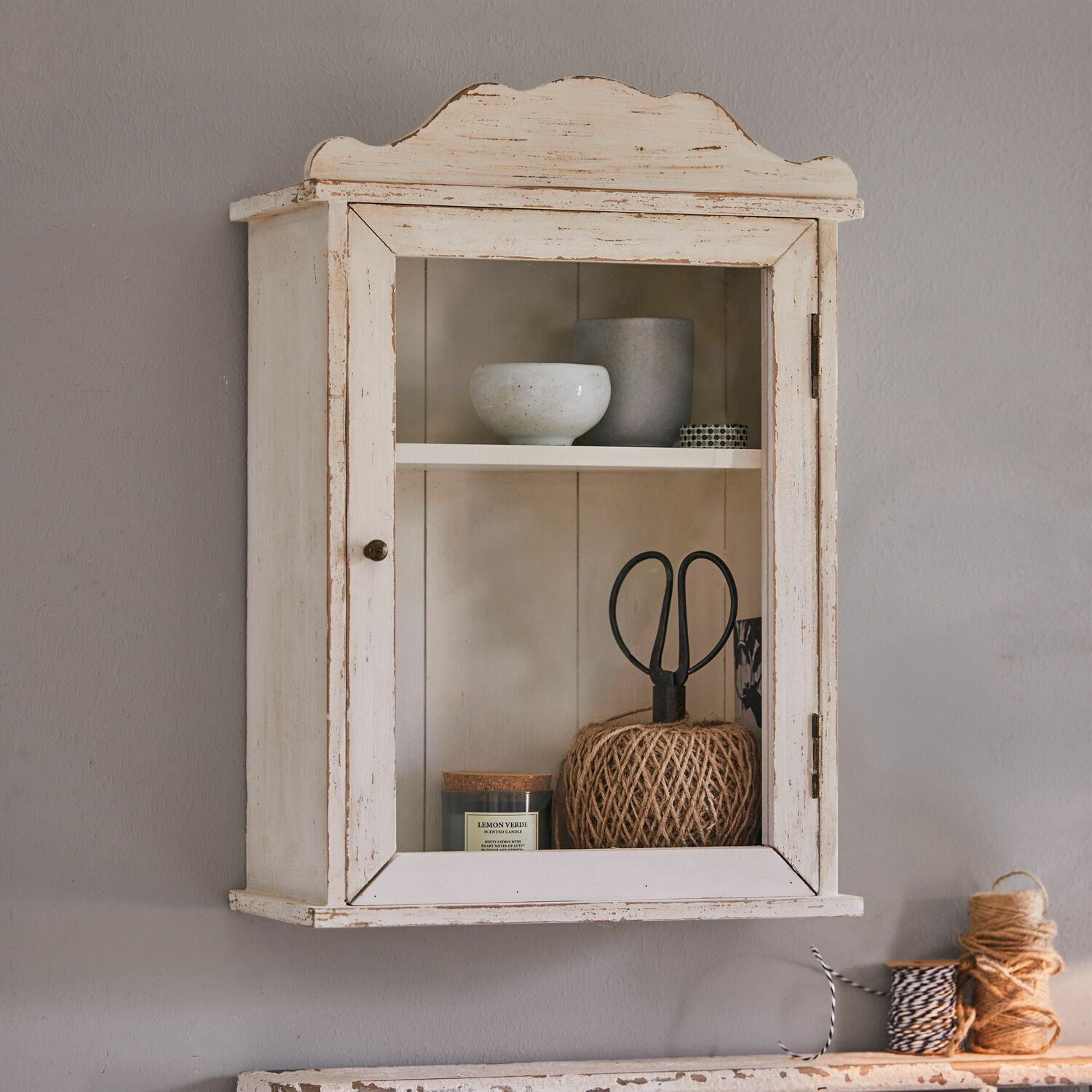 Wandschrank Sandrine Hängeschrank aus Holz im Vintage-Stil in Weiss mit Glastür und dekorativen Gegenständen innen