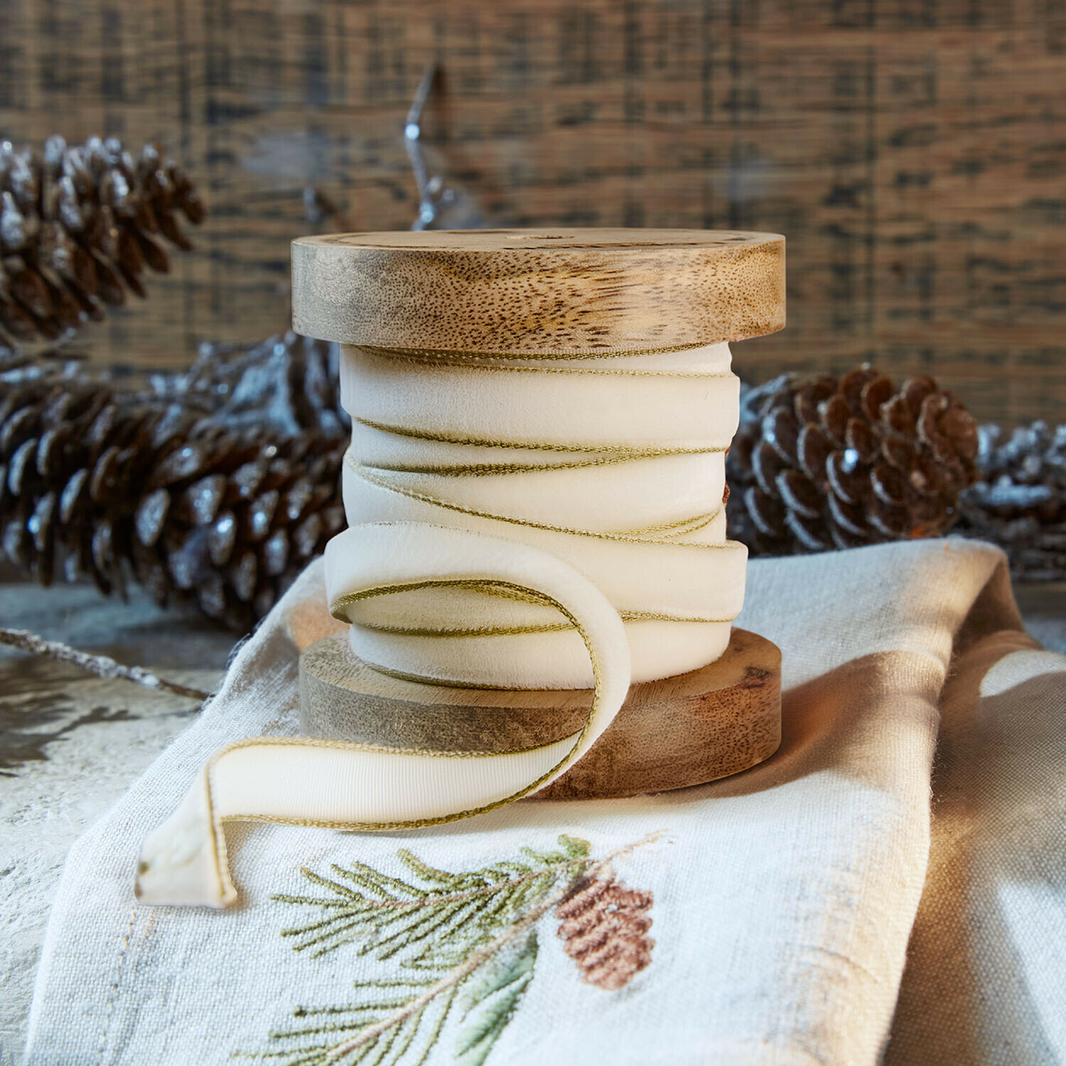 Samtband Sorima Natürliche Holzspule mit cremefarbenem Band und grünem Rand auf Leinenstoff mit Kiefernzapfen-Stickerei