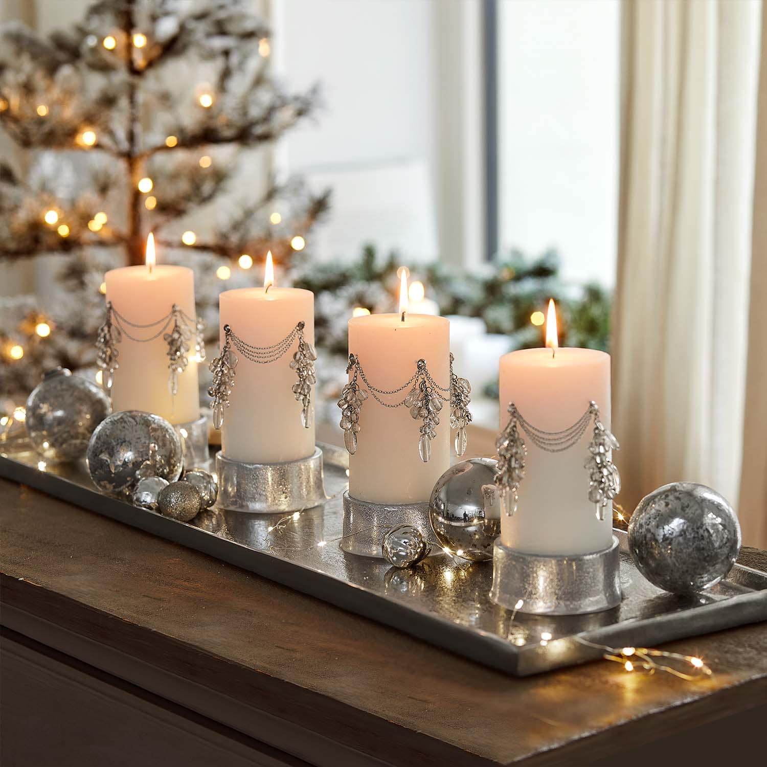 Vier weisse Kerzen mit silbernen Ketten und Kristallanhängern auf silbernem Tablett mit Weihnachtsdeko