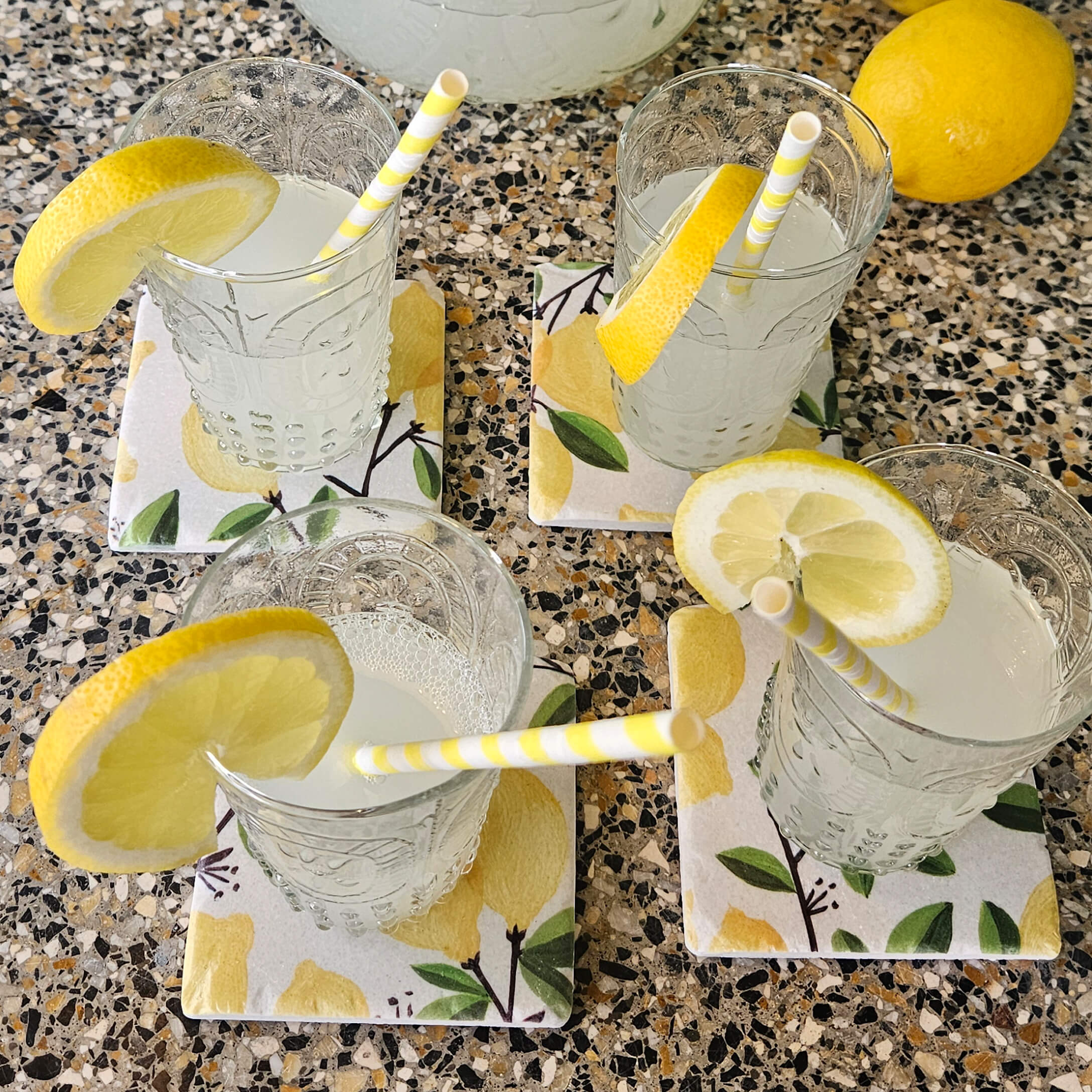 Gläser mit Limonade und Zitronenscheiben auf Keramikuntersetzern mit Zitronenmuster auf einer Steinplatte