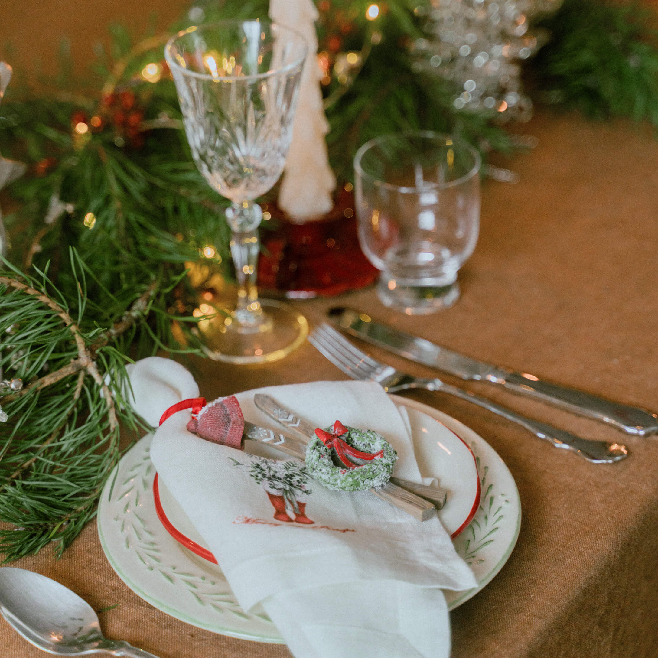 Weihnachtliche Tischdekoration mit weisser Leinenserviette, grünen Zweigen und kleinem Kranz als Dekoration