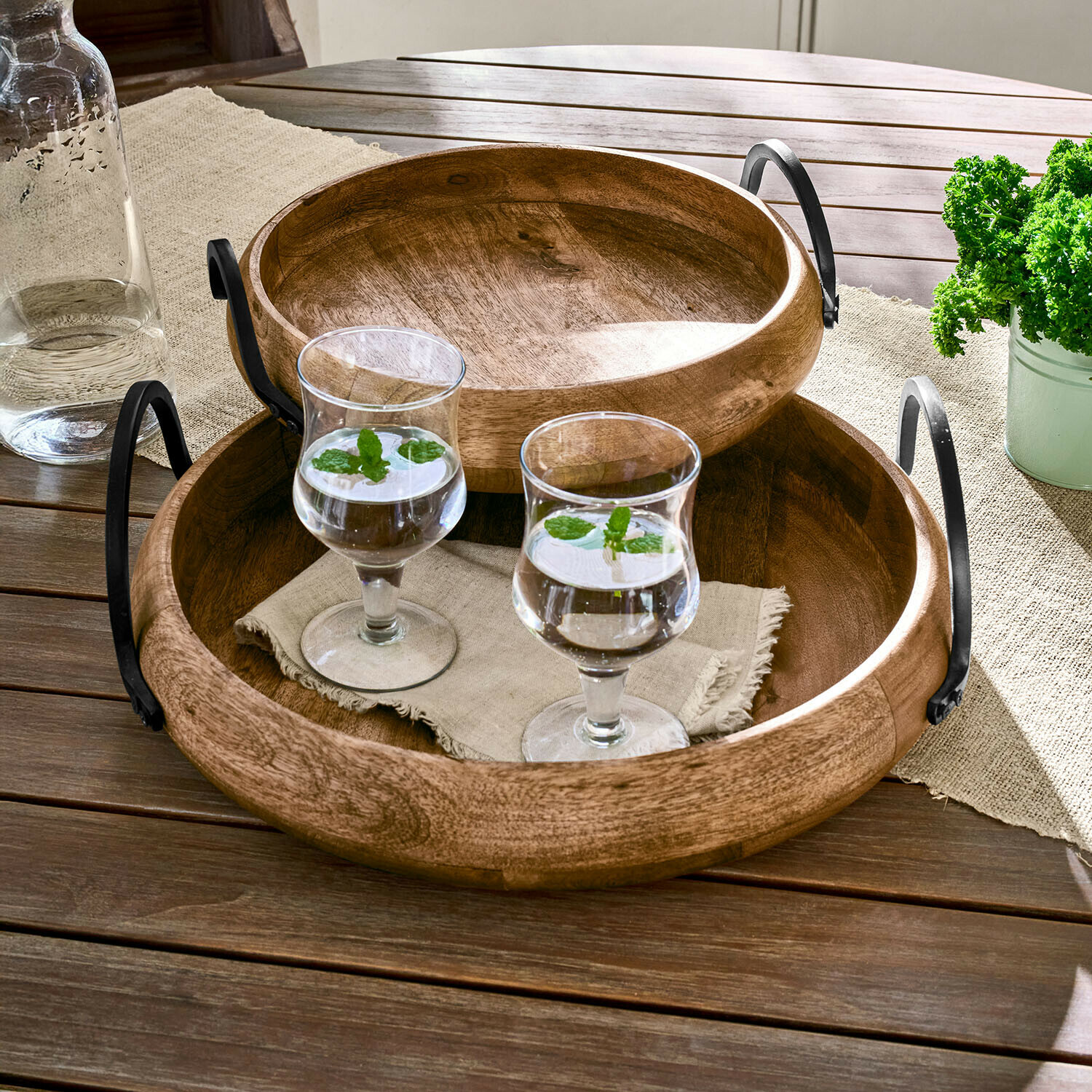 Runde Holztabletts mit Metallgriffen auf Holztisch mit zwei Gläsern Wasser und Minze