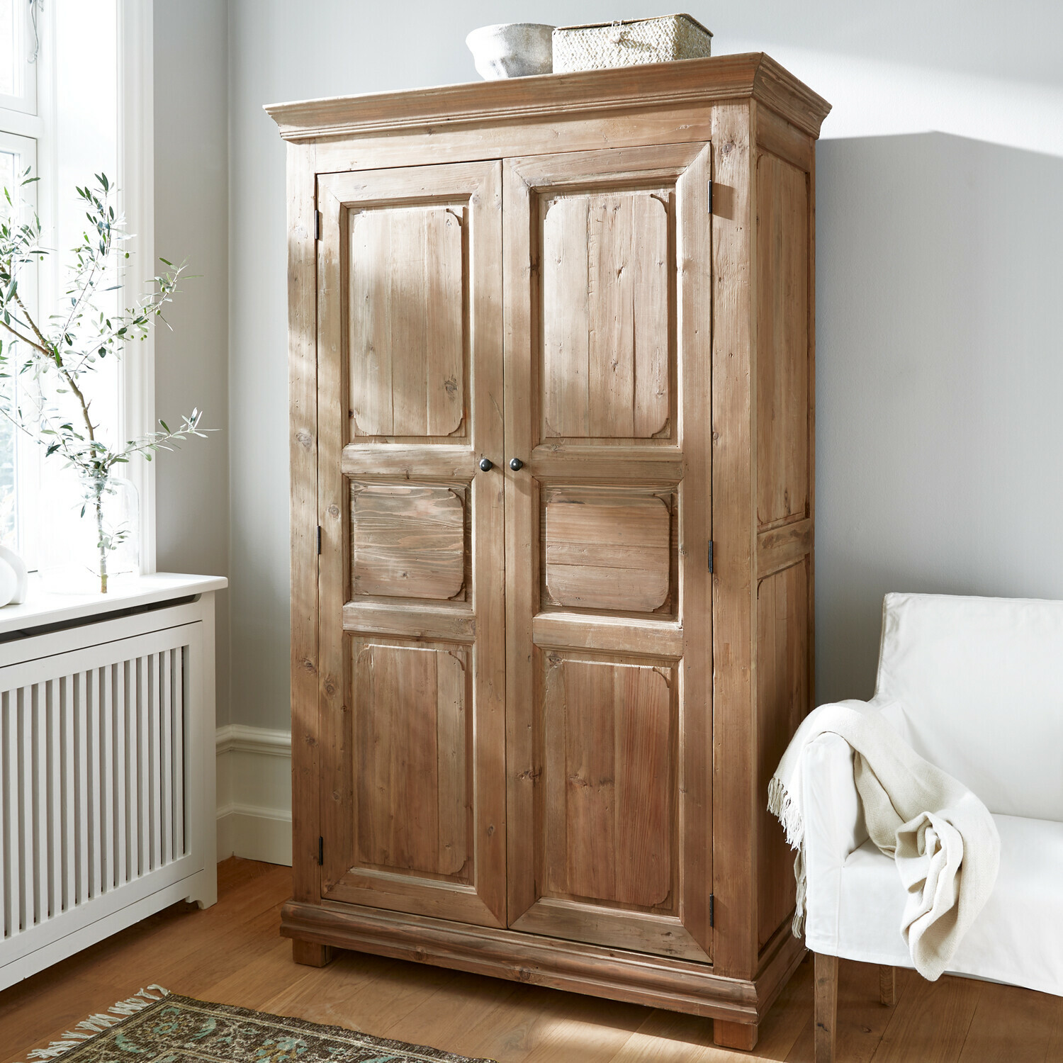 Holzschrank in Naturfarbe in hellem Zimmer mit weissem Sessel und gemustertem Teppich