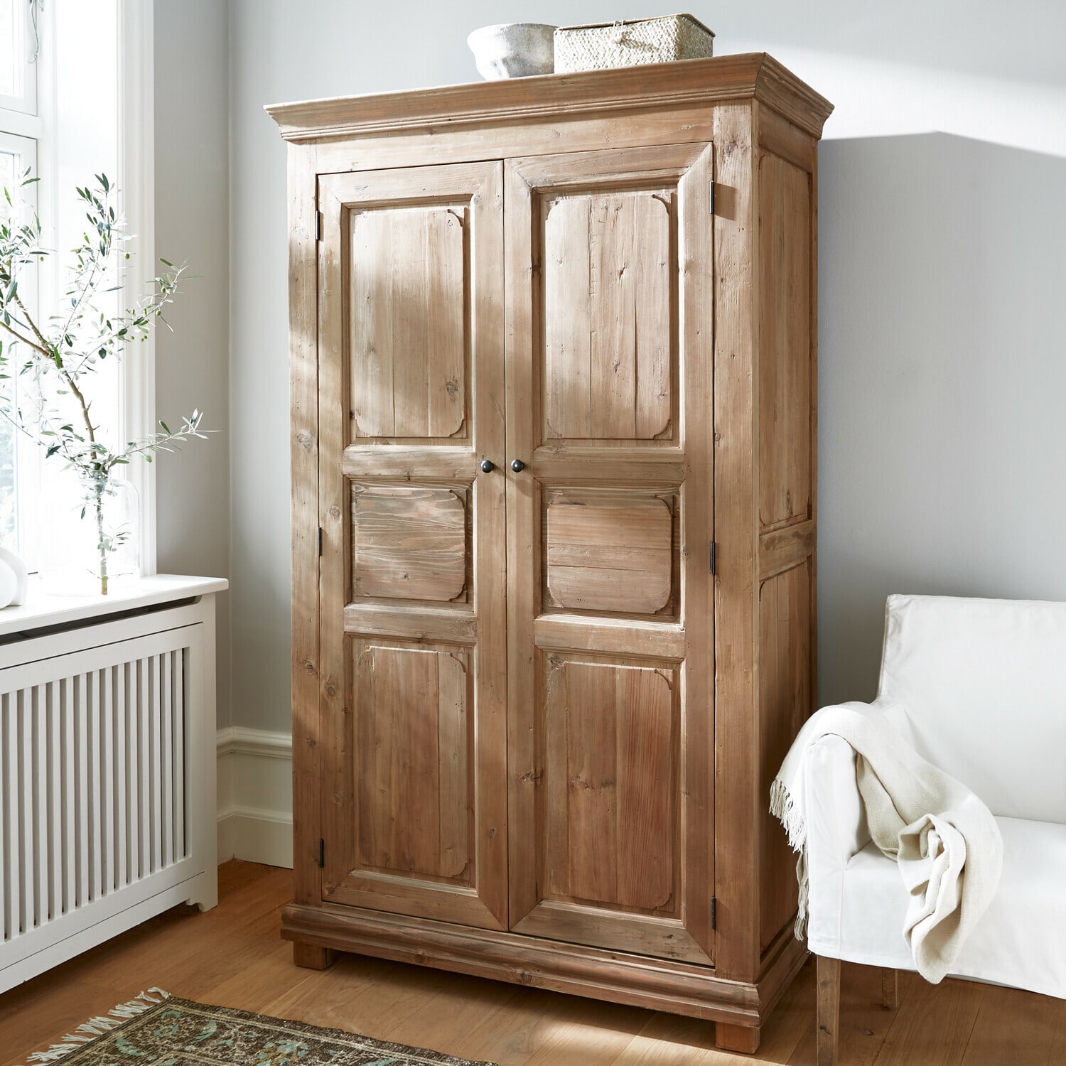Kleiderschrank Gavrielle Holzschrank in Naturfarbe in hellem Zimmer mit weissem Sessel und gemustertem Teppich
