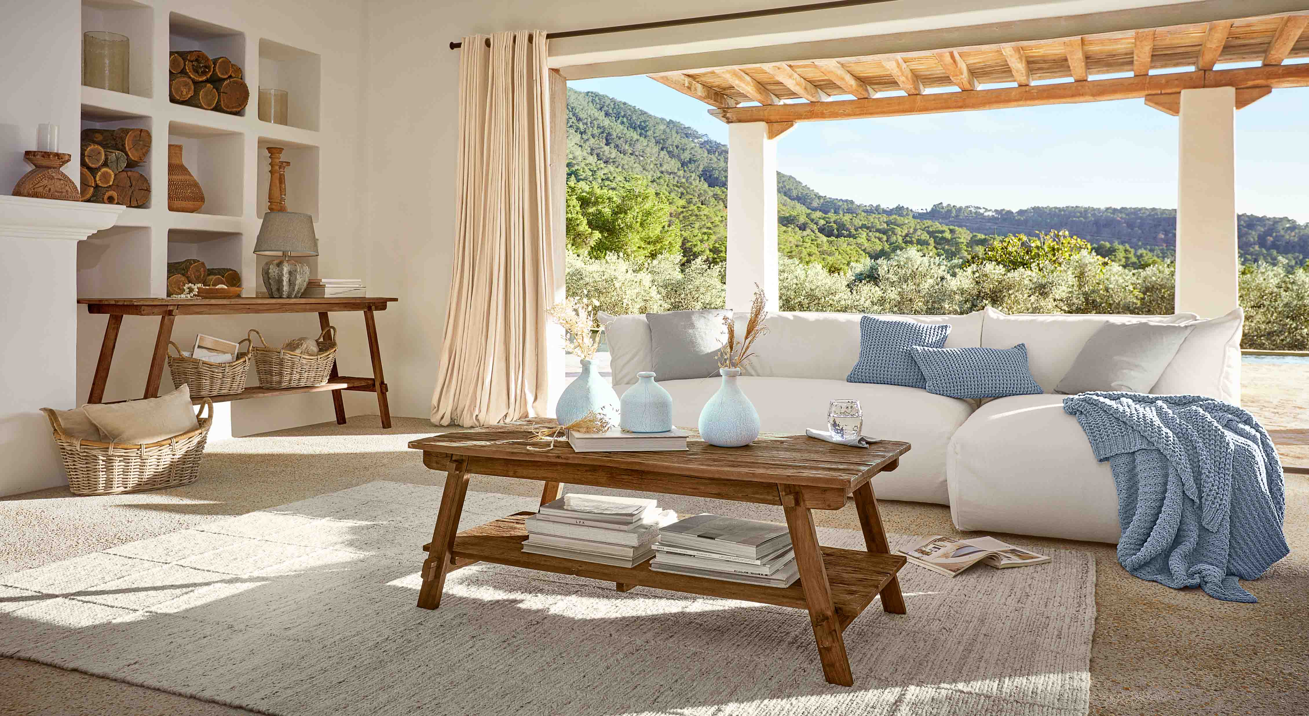 Wohnzimmer mit Holztisch, weissem Sofa und blauem Plaid, natürliche Dekoration und Aussicht ins Grüne