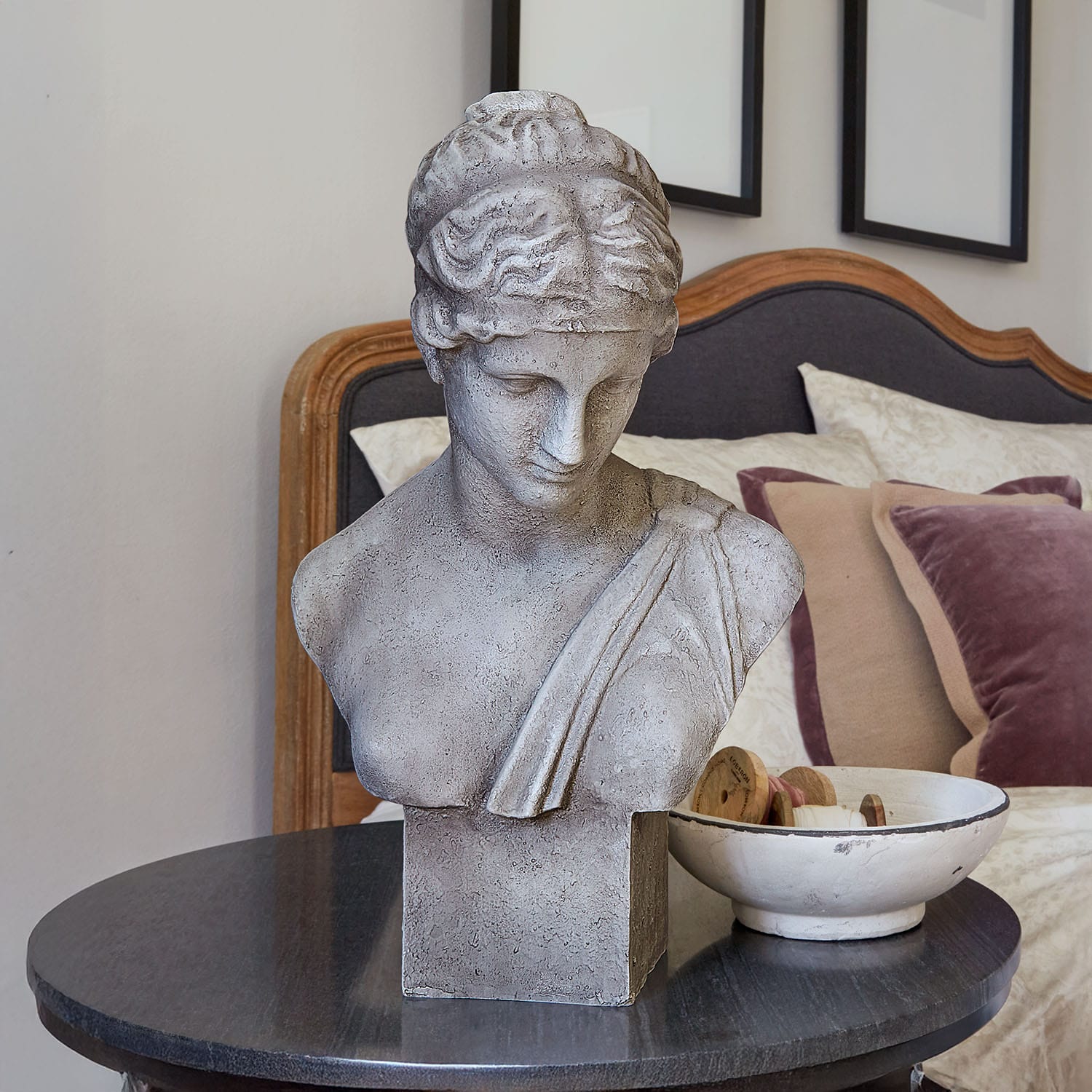 Graue Steinskulptur-Büste auf schwarzem Tisch in stilvollem Schlafzimmer mit Kissen