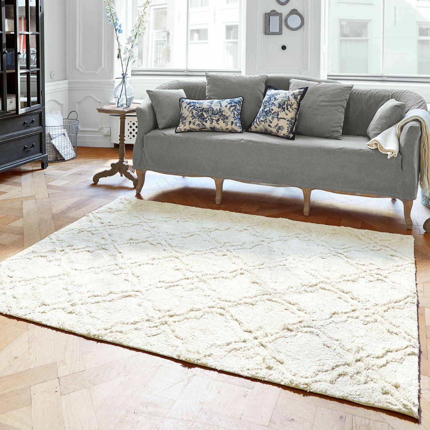Teppich Petrus Heller Teppich aus weichem Material mit geometrischem Muster im modernen Wohnzimmer mit grauem Sofa.