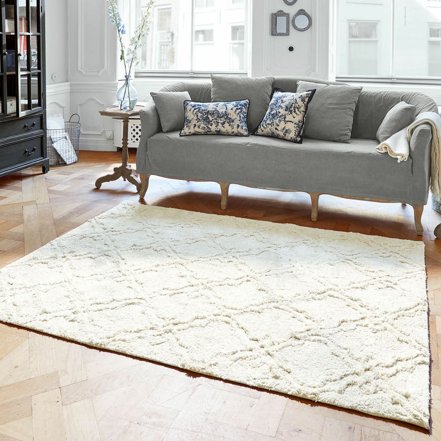 Teppich Petrus Heller Teppich aus weichem Material mit geometrischem Muster im modernen Wohnzimmer mit grauem Sofa.