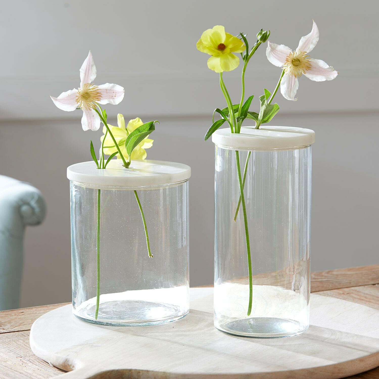 Glasdose 2er Set Rosanella Zwei transparente Glasvasen mit weissen Deckeln und hellen Blumen auf einem Holztisch