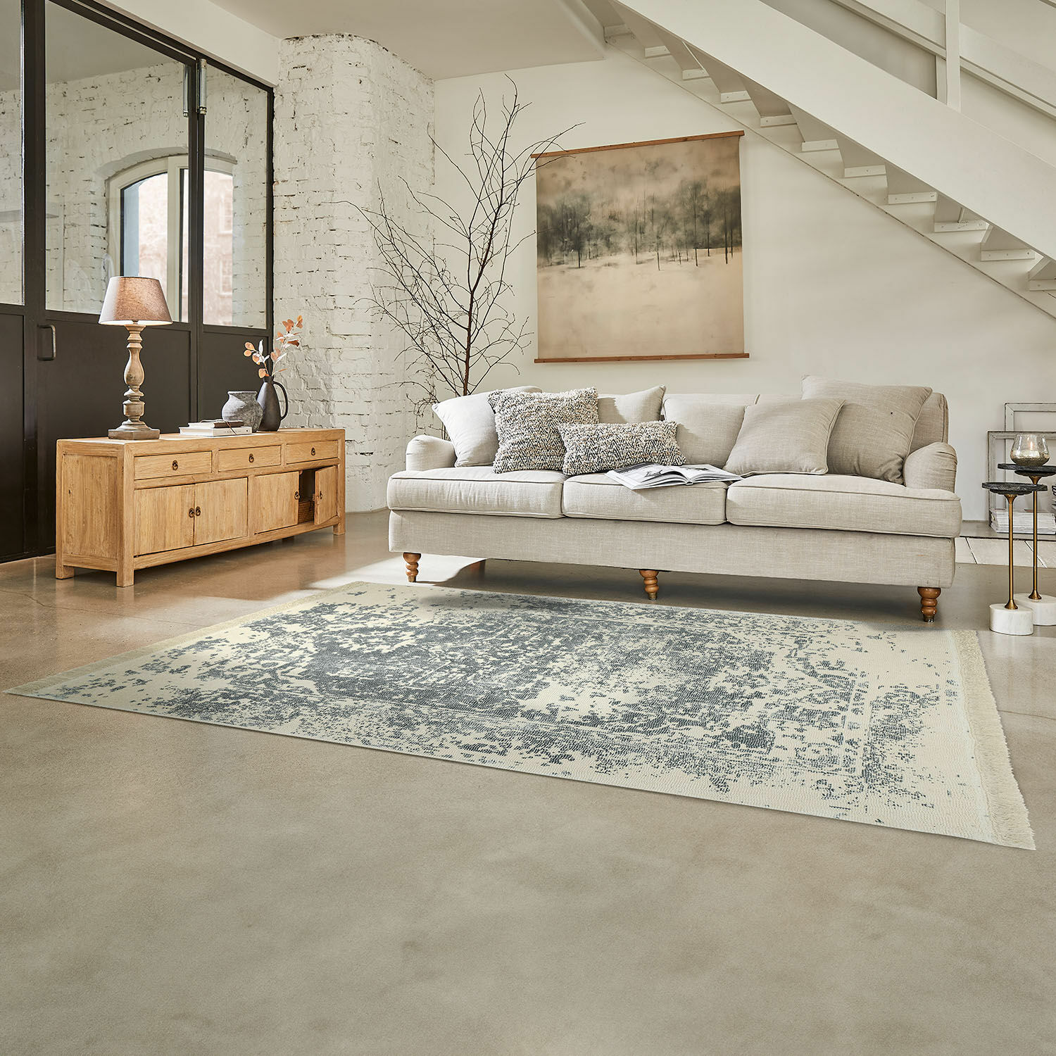Teppich Lortet Beiges Sofa mit Kissen auf grauem Teppich in hellem Wohnzimmer mit Holzkommode und Wanddekoration