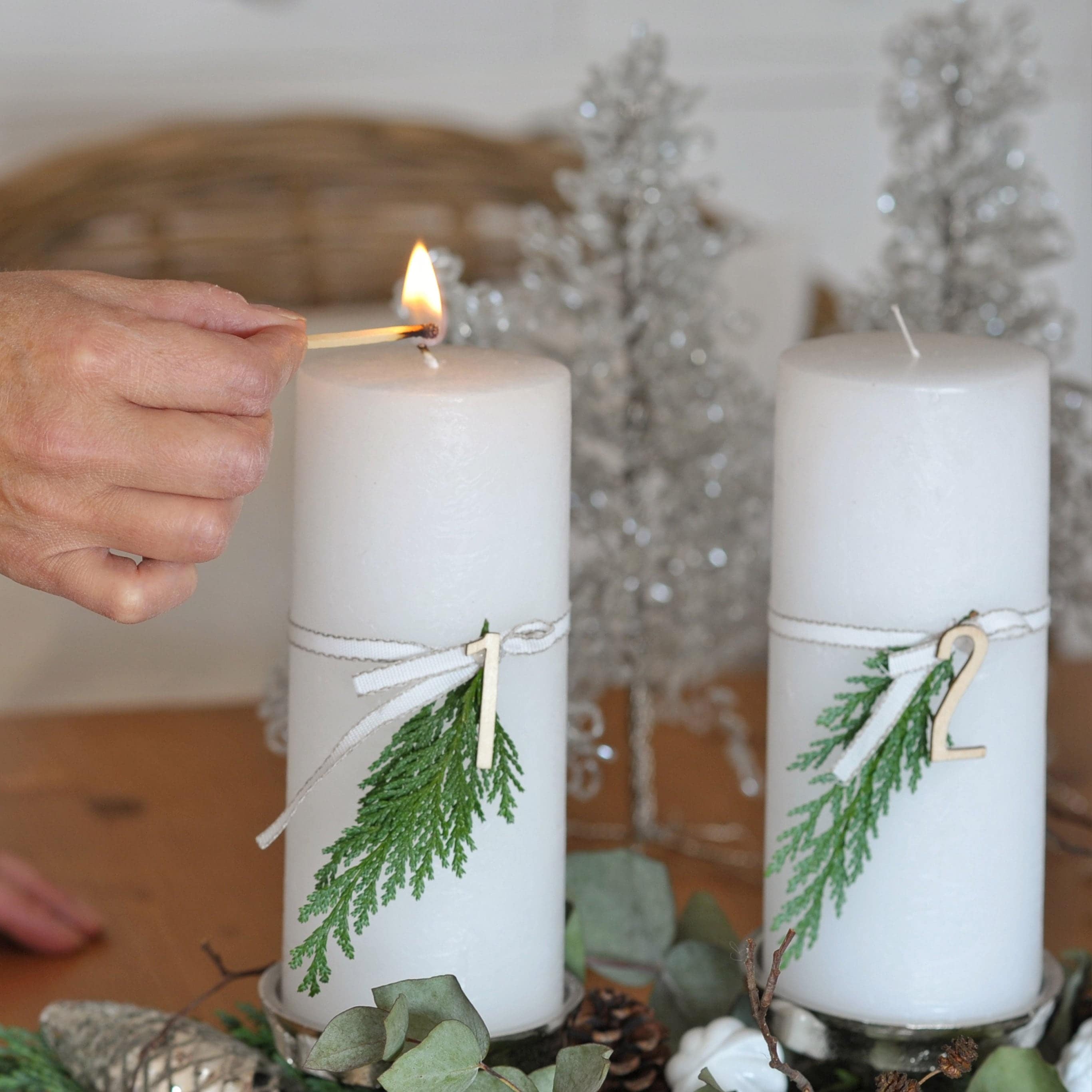 Weisse Adventskerzen mit grünen Zweigen und Holznummern auf dekorativem Weihnachtstablett