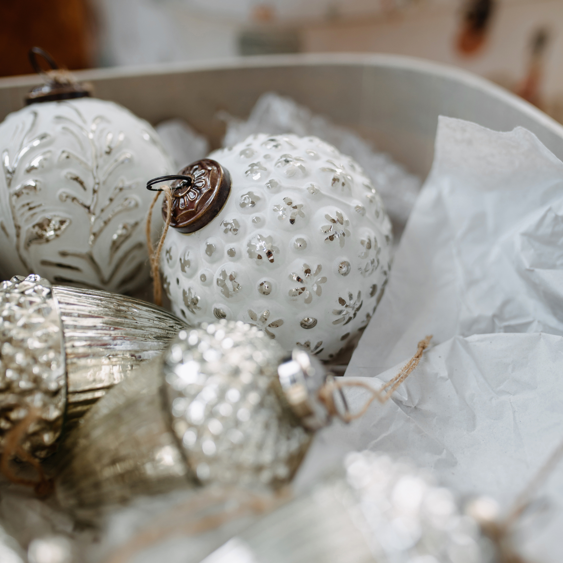 Weisse und silberne Weihnachtskugeln aus Glas und Metall mit Mustern in einer Schachtel mit Papier