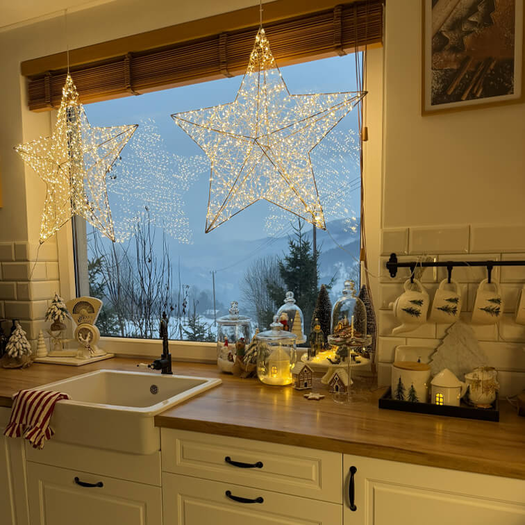 Leuchtende Stern-Dekorationen in der Küche mit Holzarbeitsplatte und Weihnachtsdeko vor winterlicher Aussicht
