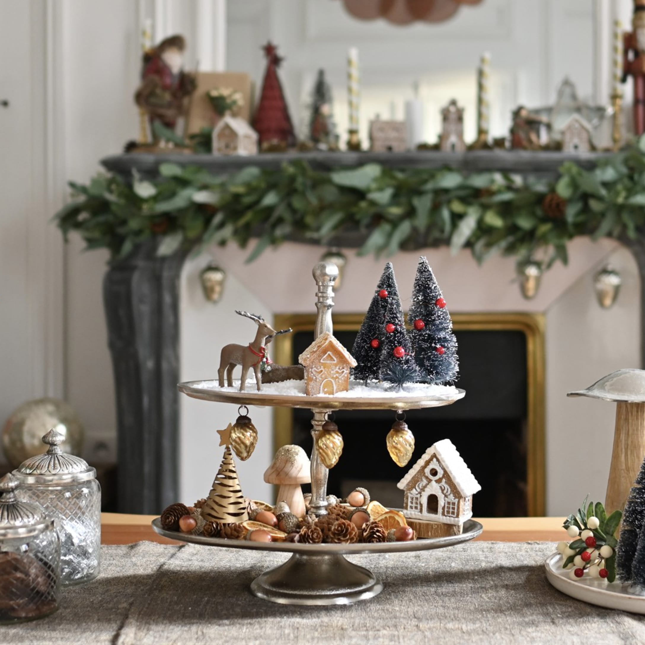 Zweistöckige Metalletagere mit Weihnachtsdekorationen und Lebkuchenhäusern auf dem Tisch