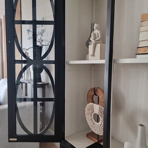 Schwarze Metallvitrine mit dekorativen Regalen und Skulpturen im hellen Wohnzimmer