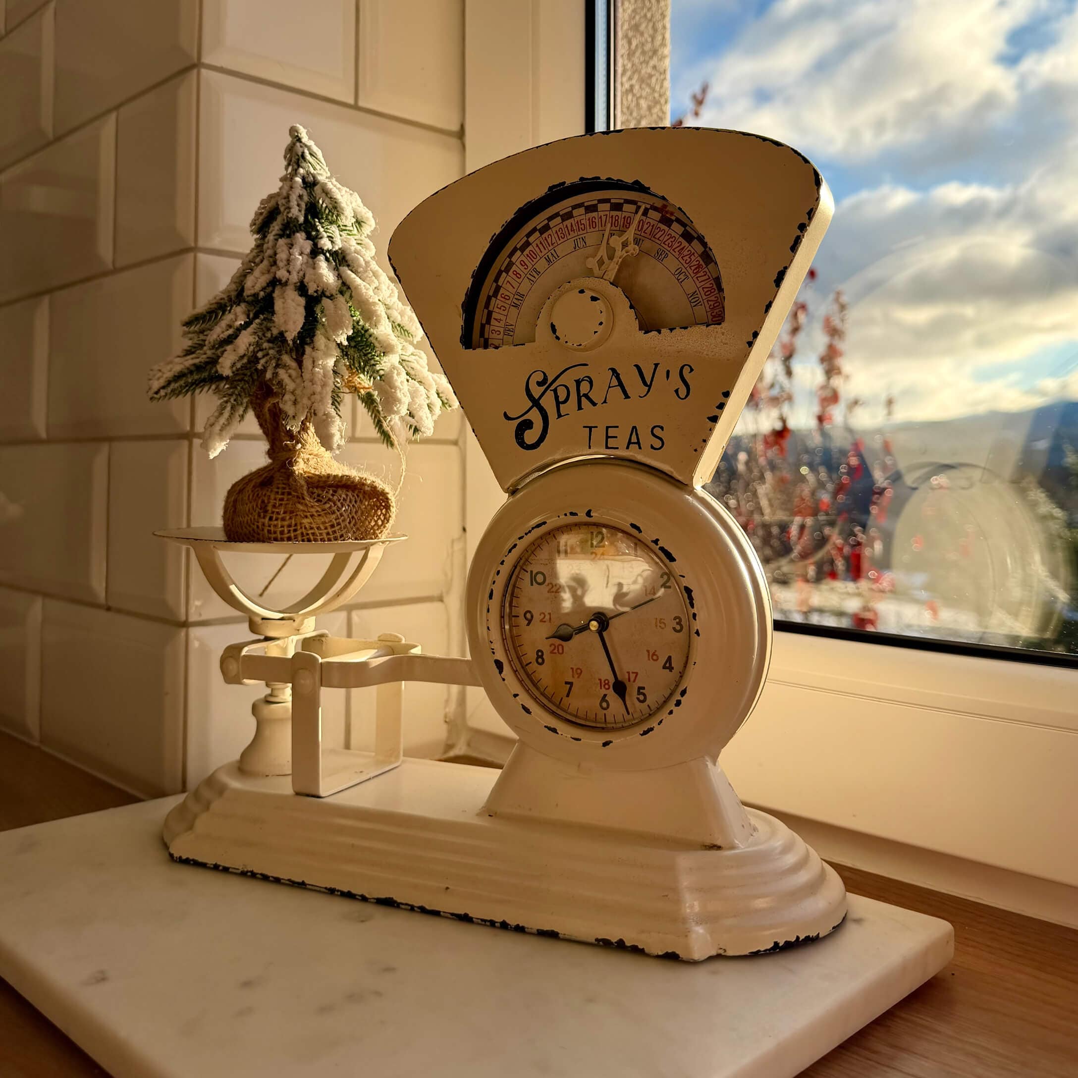 Beige Metall-Küchenwaage mit Uhr und Weihnachtsdekoration auf Fensterbank im warmen Licht