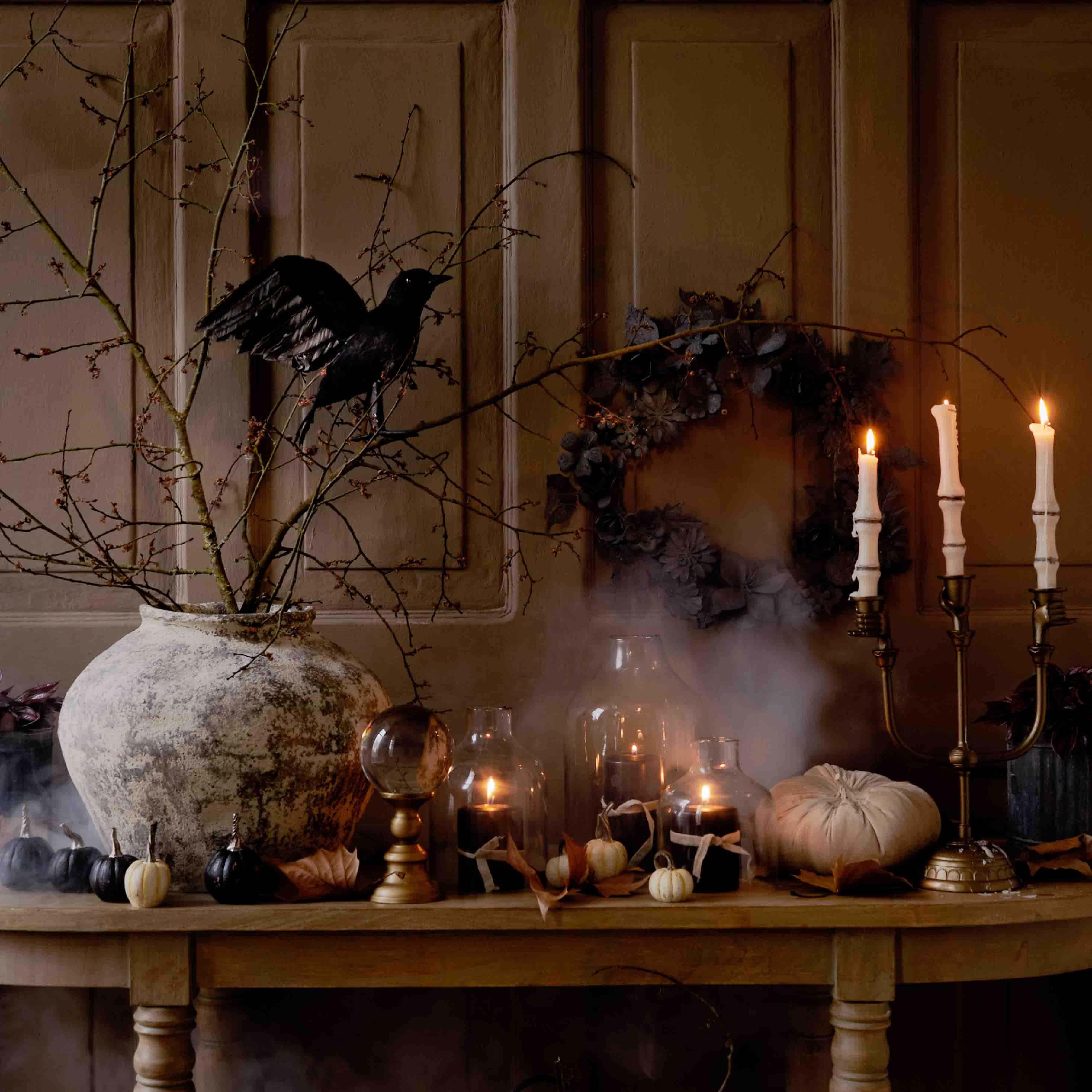 Herbstliche Tischdekoration mit grossem Keramikvase, brennenden Kerzen und schwarzem Vogel auf Zweig