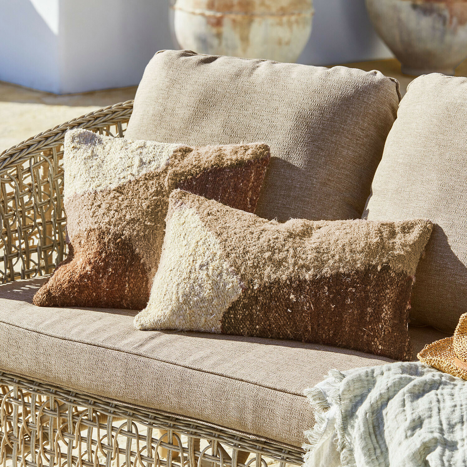 Beiges Rattansofa mit weichen Kissen in Braun- und Cremetönen, dekorative textile Decke