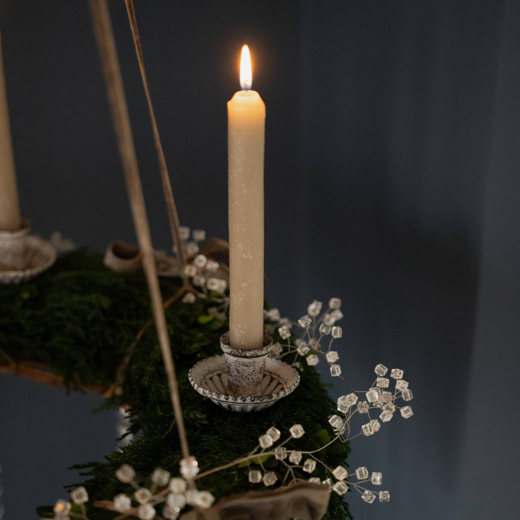 Detailaufnahme einer brennenden Kerze auf einem grünen Adventskranz mit Kristalldekor vor dunklem Hintergrund